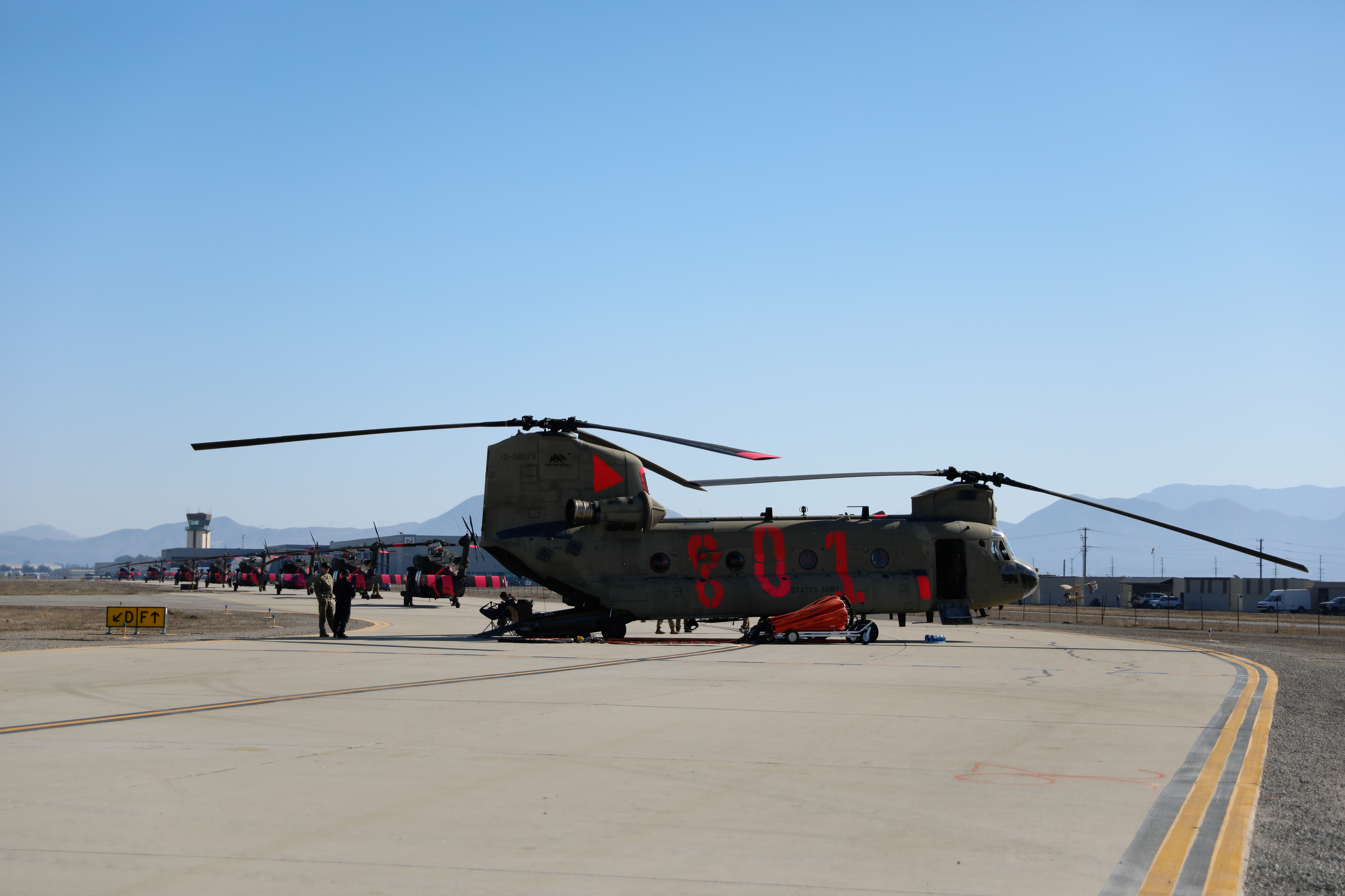 Military helicopter on an airport tarmac with mountains visible in the background.