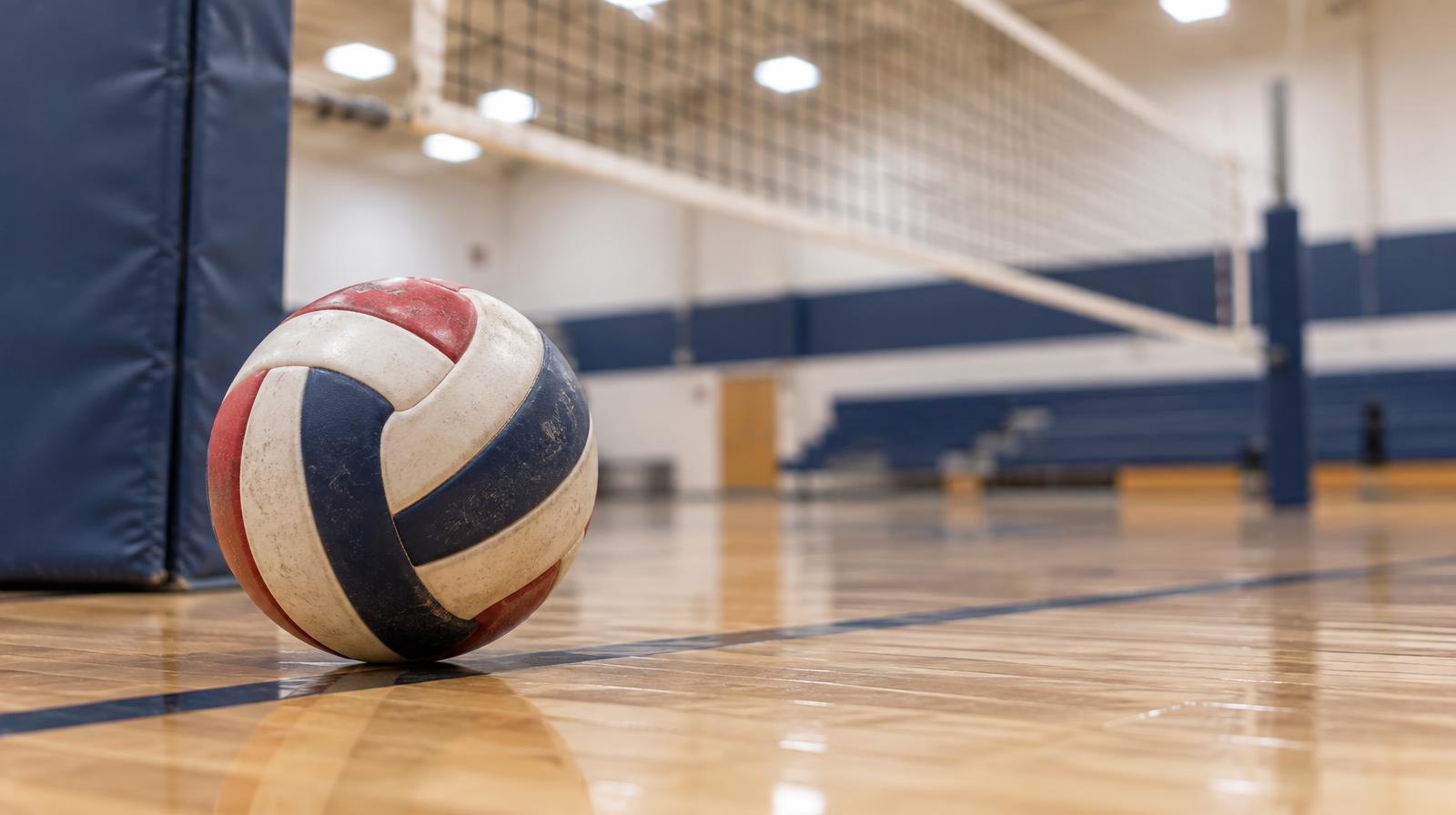 A volleyball resting on a hardwood gymnasium floor near the net post.