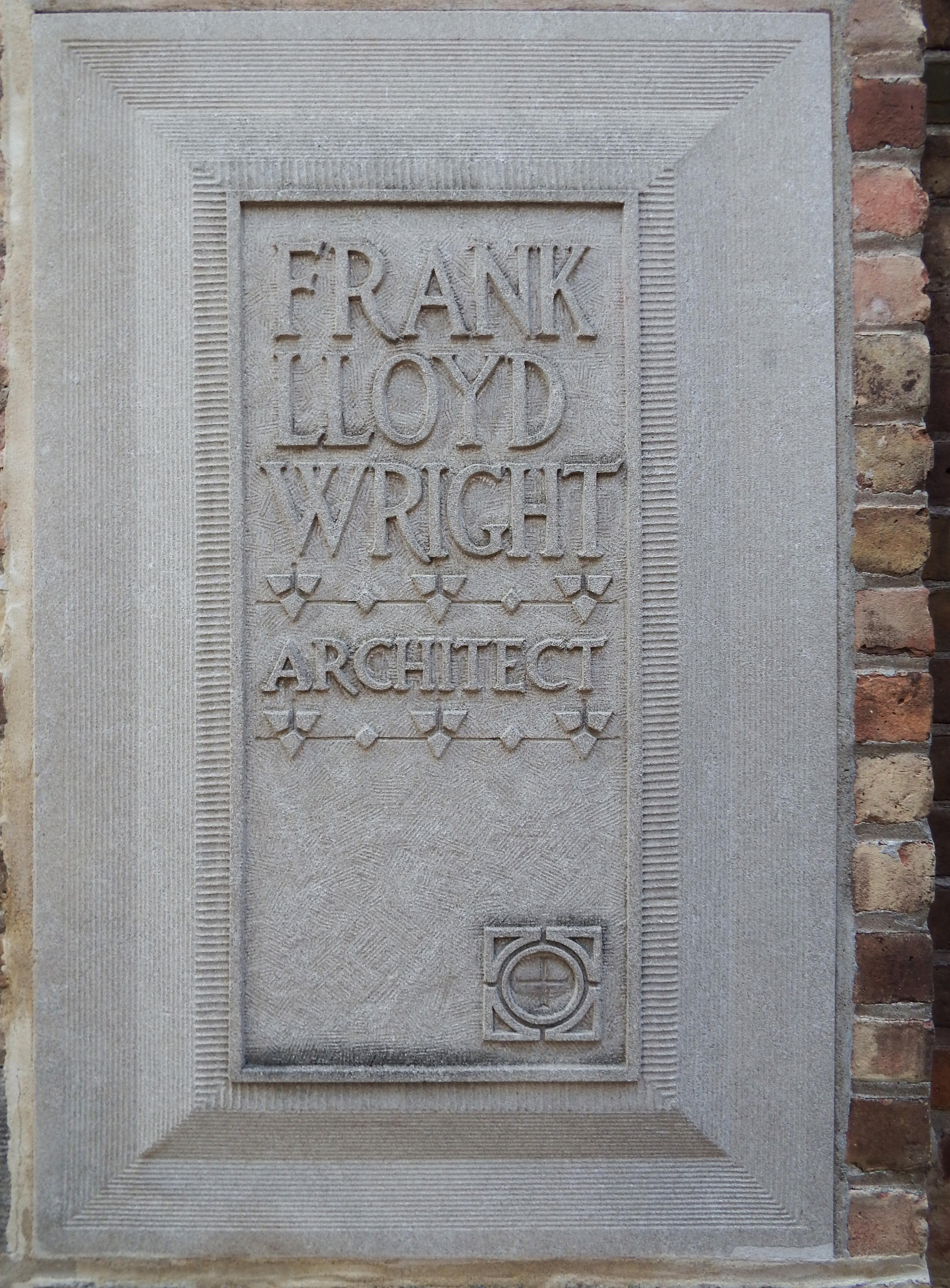 Carved stone marker reading Frank Lloyd Wright Architect set into a brick wall.