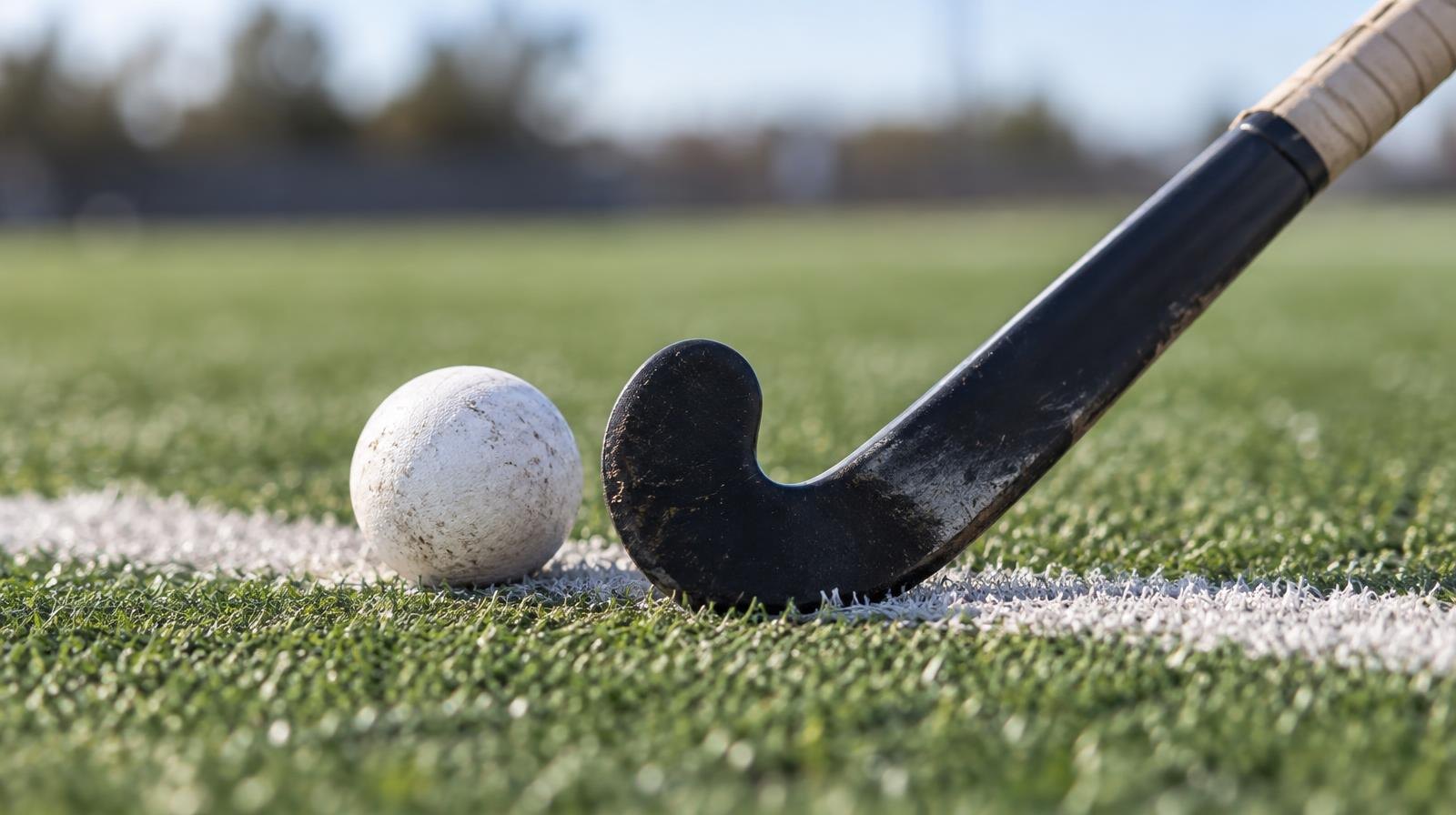 A field hockey stick and ball resting on green artificial turf near a white line.