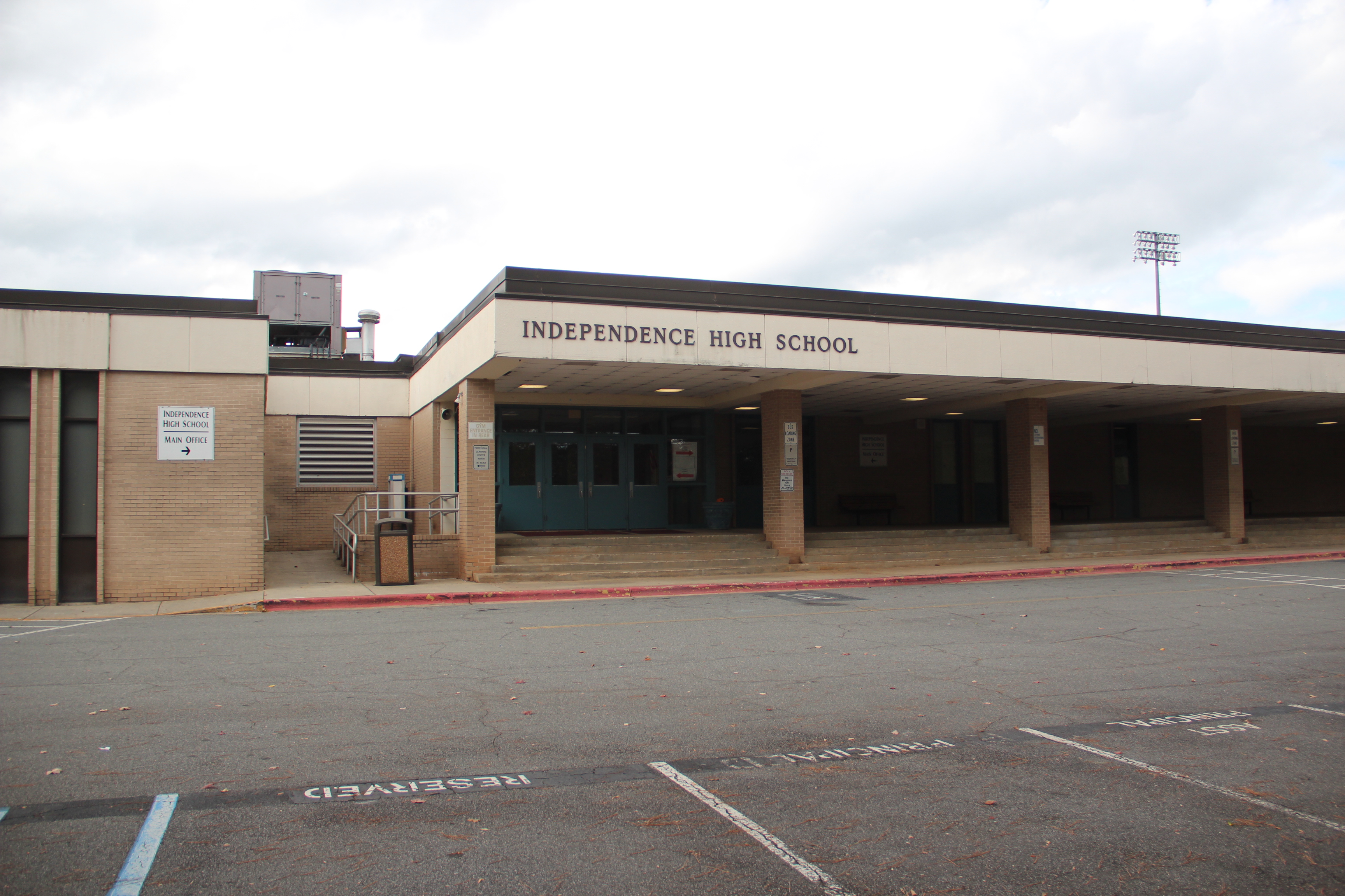 Single-story brick school building with covered entrance, school sign, and parking lot in front.