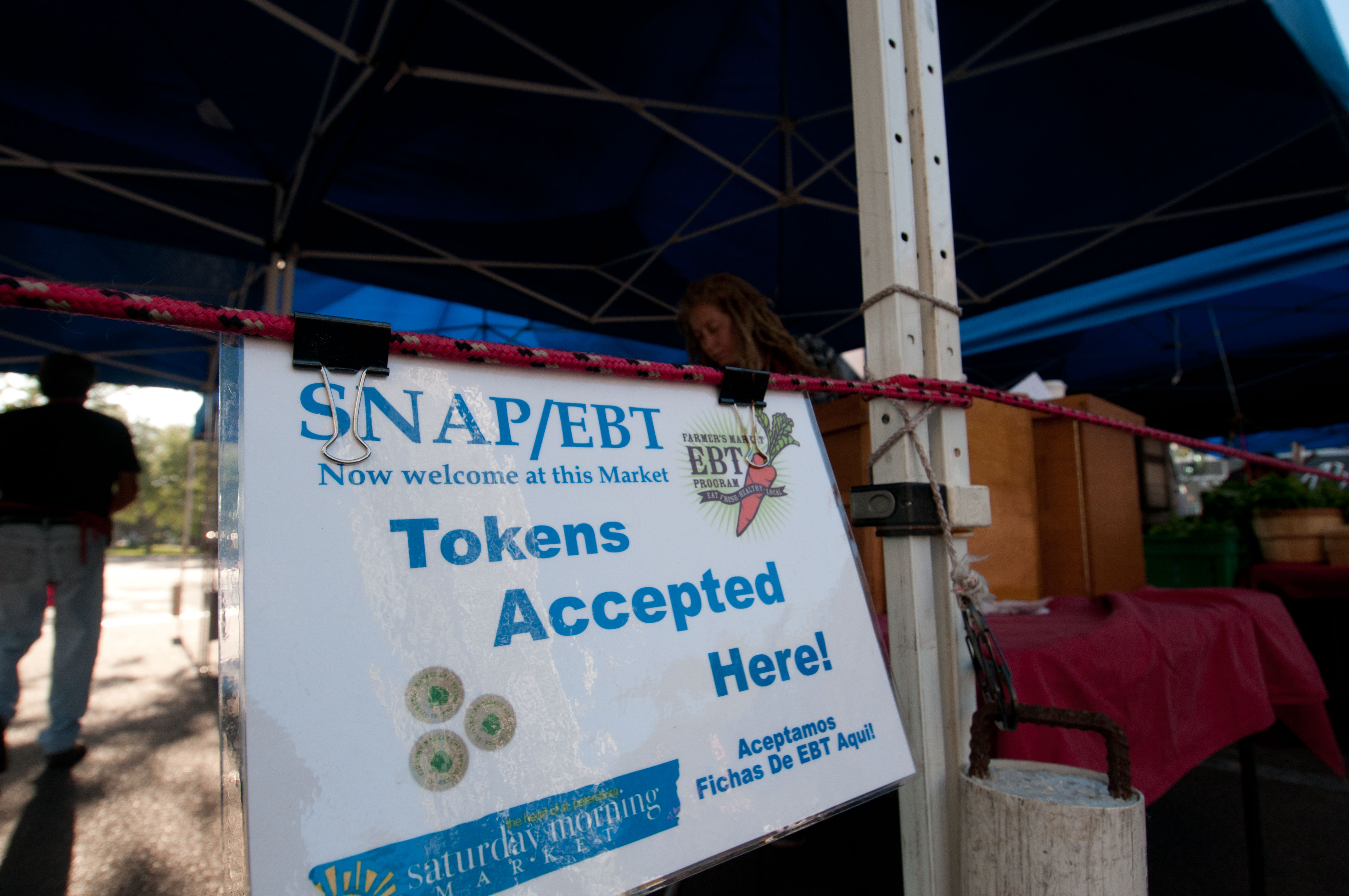 Bilingual sign at an outdoor market booth reading 'SNAP/EBT Tokens Accepted Here.'