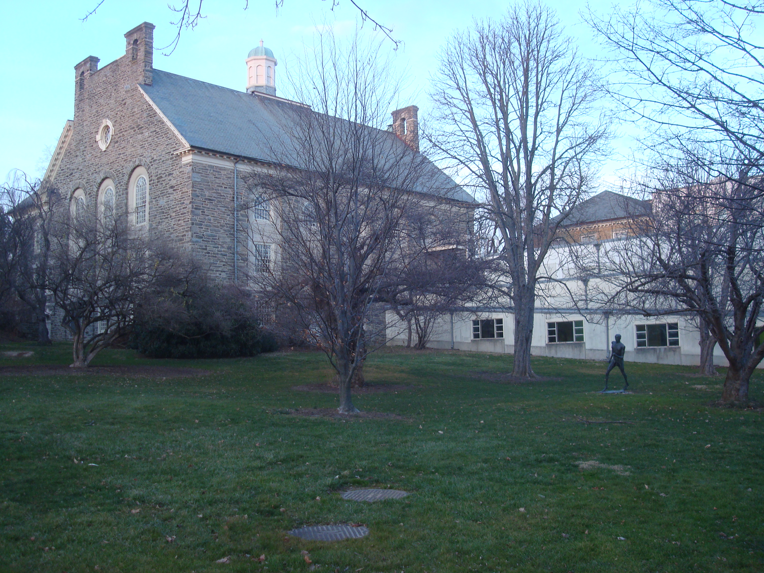 Stone Gothic-style college building with arched windows surrounded by bare winter trees.