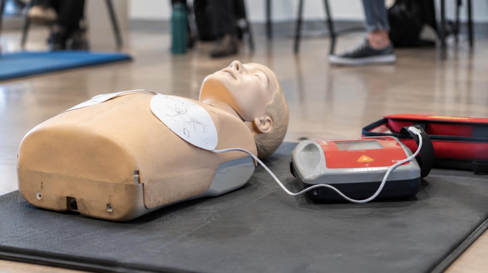 CPR training mannequin on a mat with an AED training device beside it.