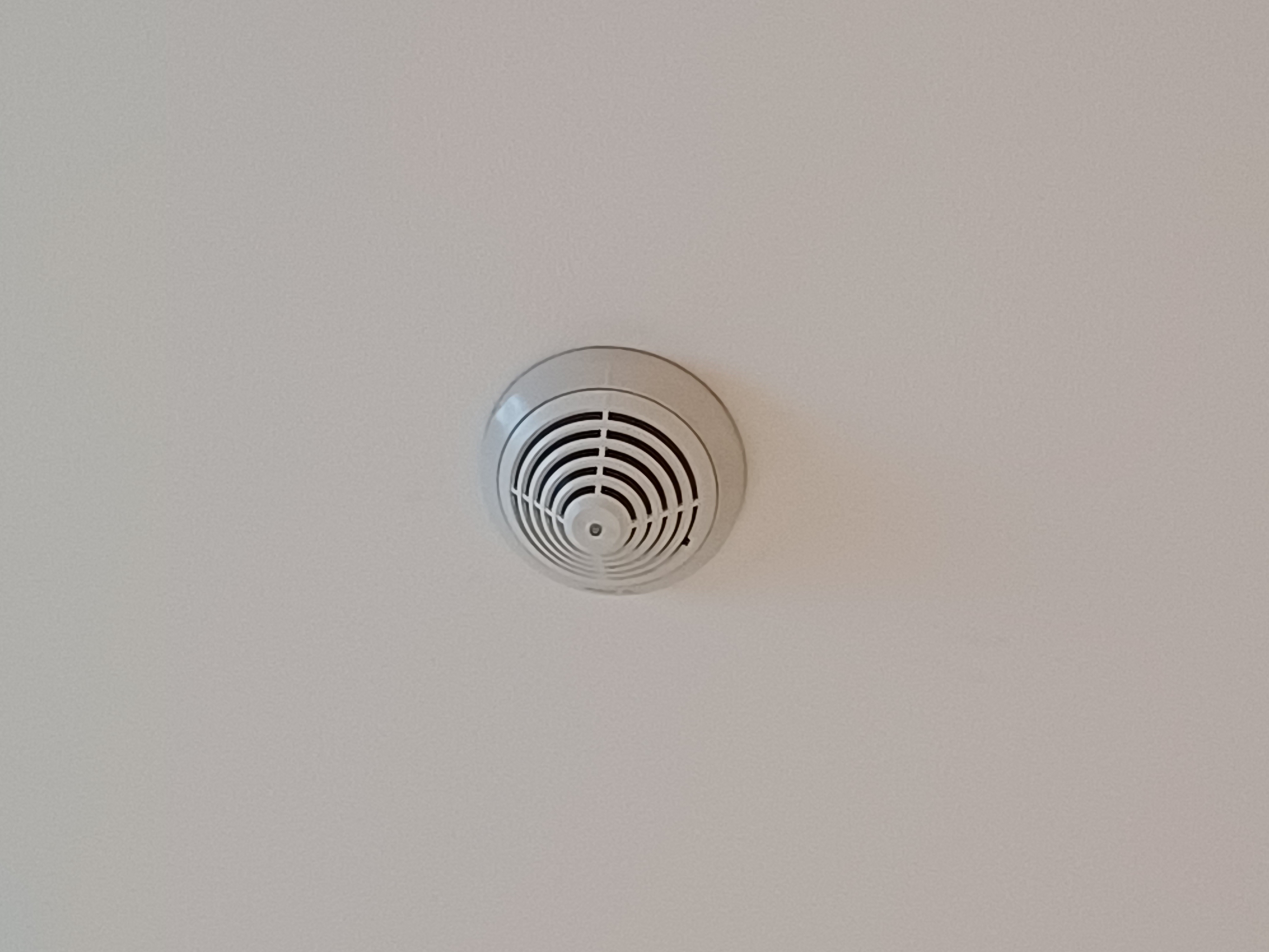 A white circular smoke detector mounted flush on a white ceiling.