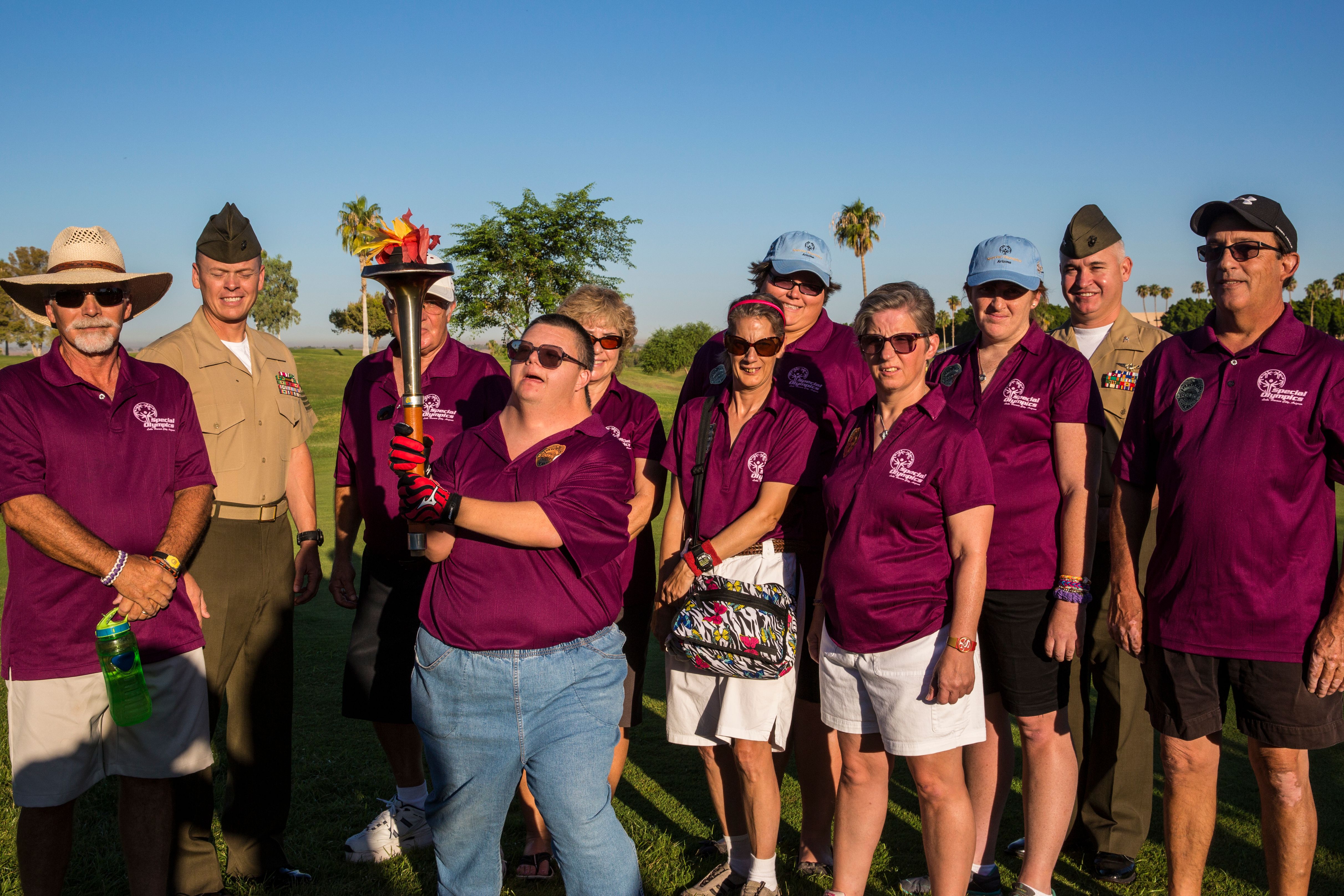 Group of athletes in matching polo shirts posing with supporters on a sunny golf course.
