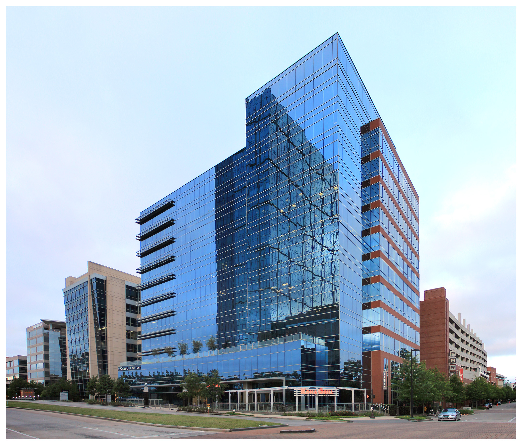 Multi-story glass office building with blue reflective curtain wall at a street corner.