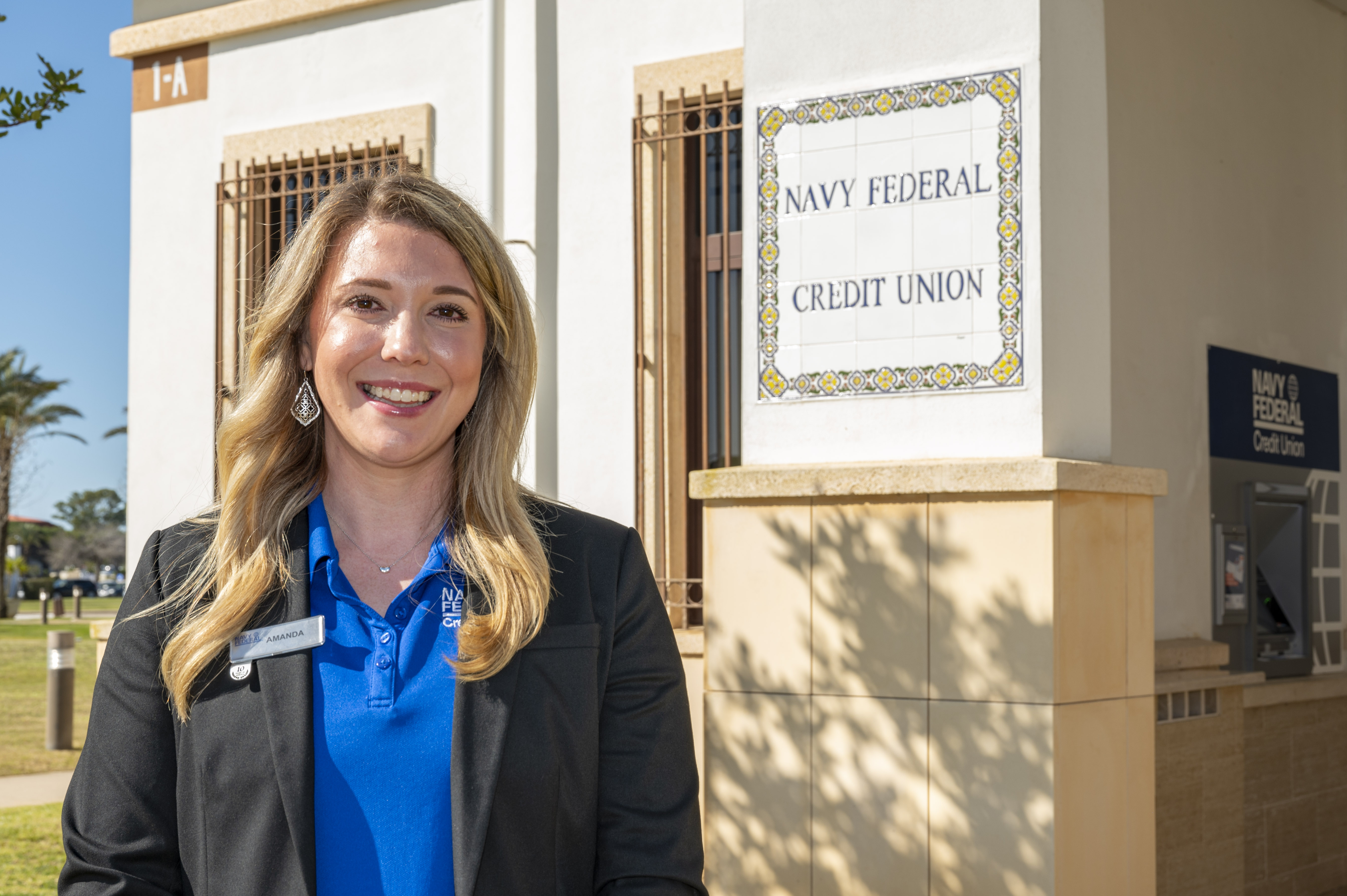 A woman smiling in front of a Navy Federal Credit Union branch building with decorative tile signage.