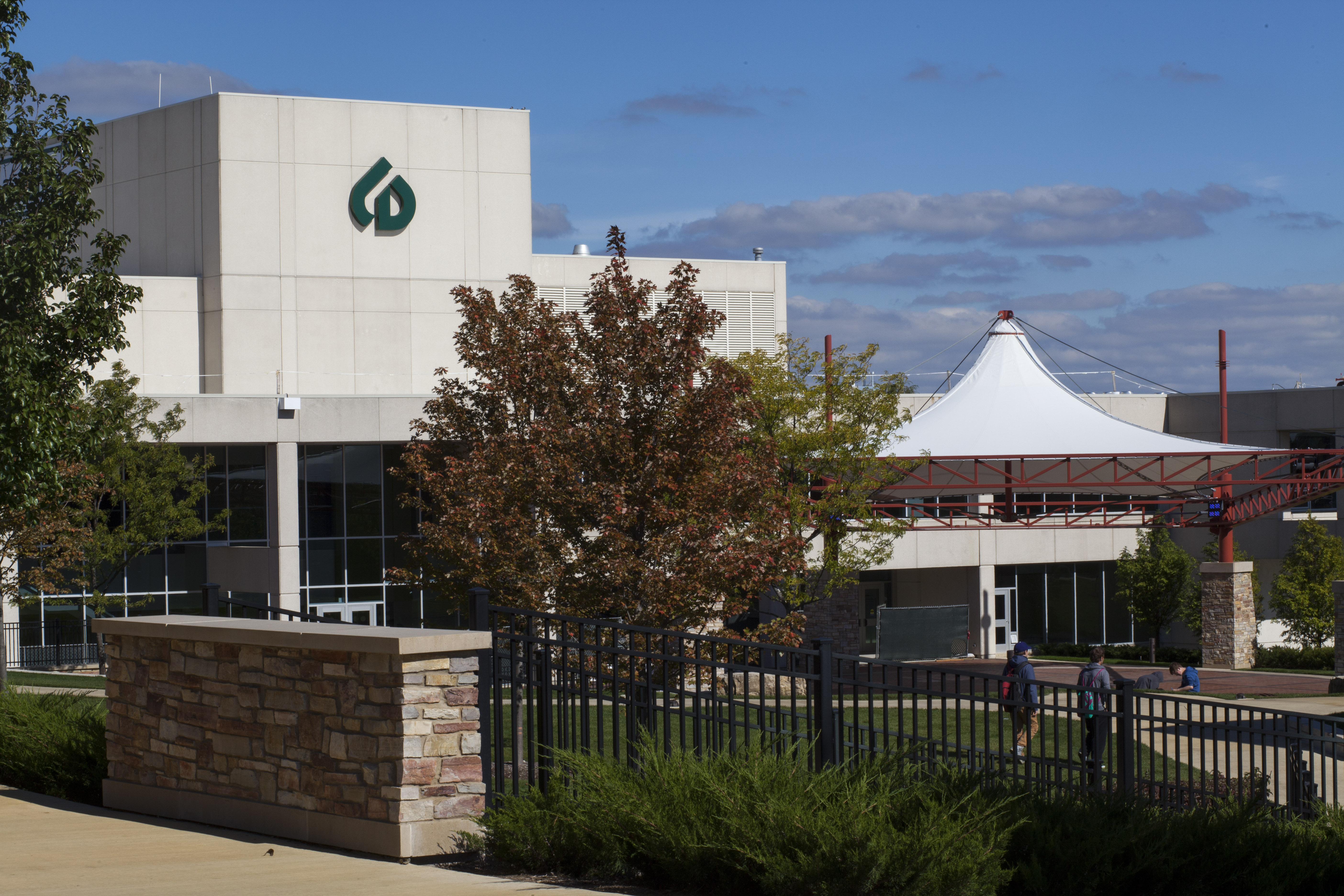 Exterior of a college arts center building with courtyard, autumn trees, and a white tent canopy.