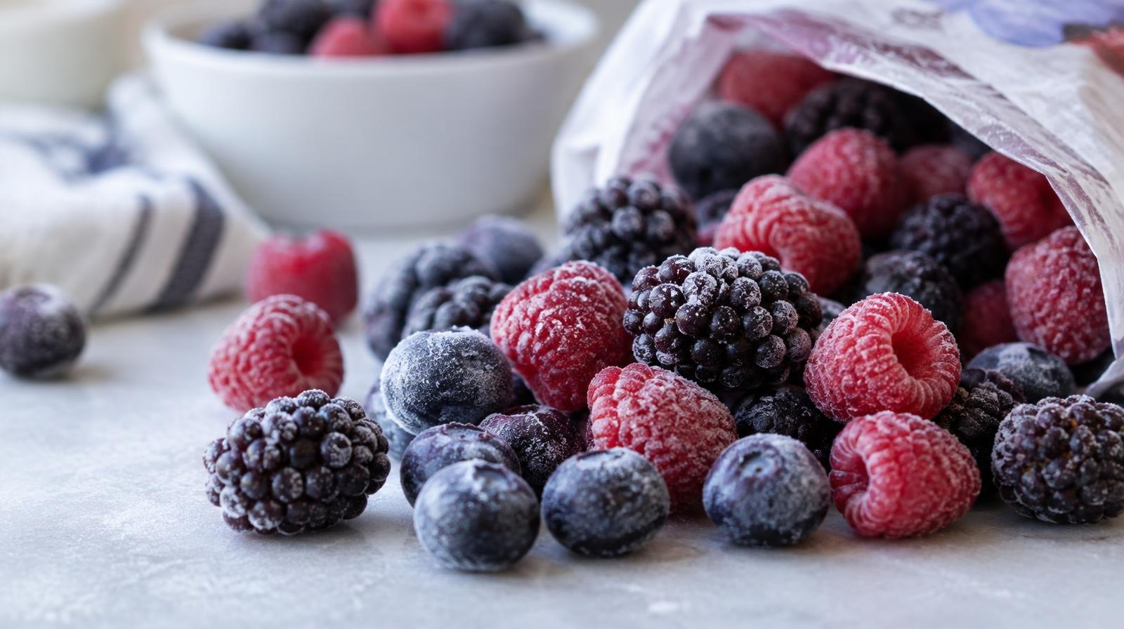 Frozen blueberries, raspberries, and blackberries spilling from a bag onto a white surface.