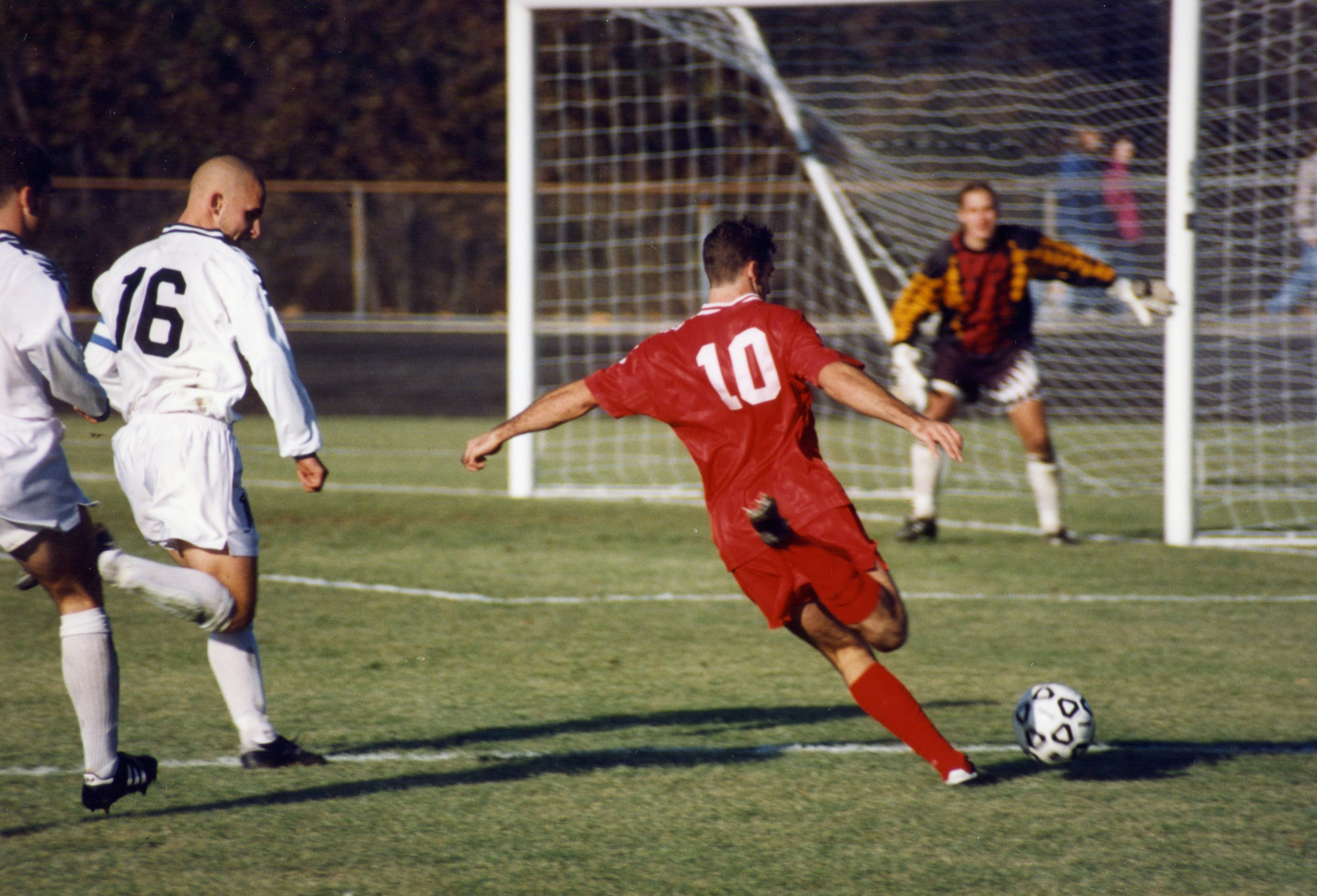Soccer player in red jersey sprinting past two defenders toward a goal.