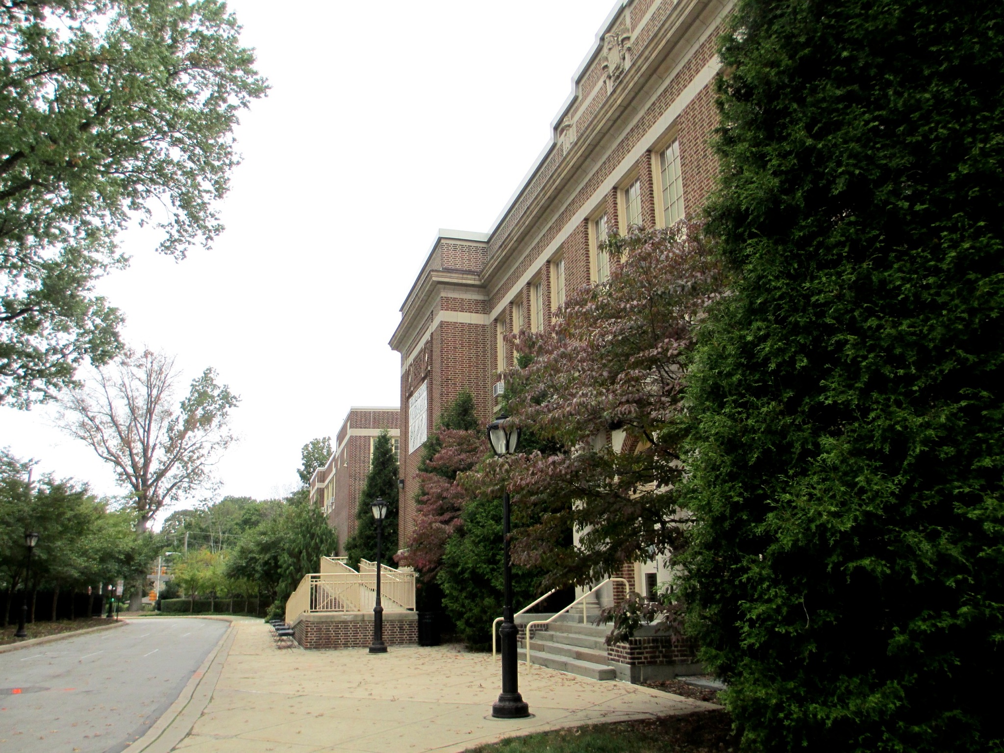 Multi-story red brick school building with tall windows and a tree-lined walkway.