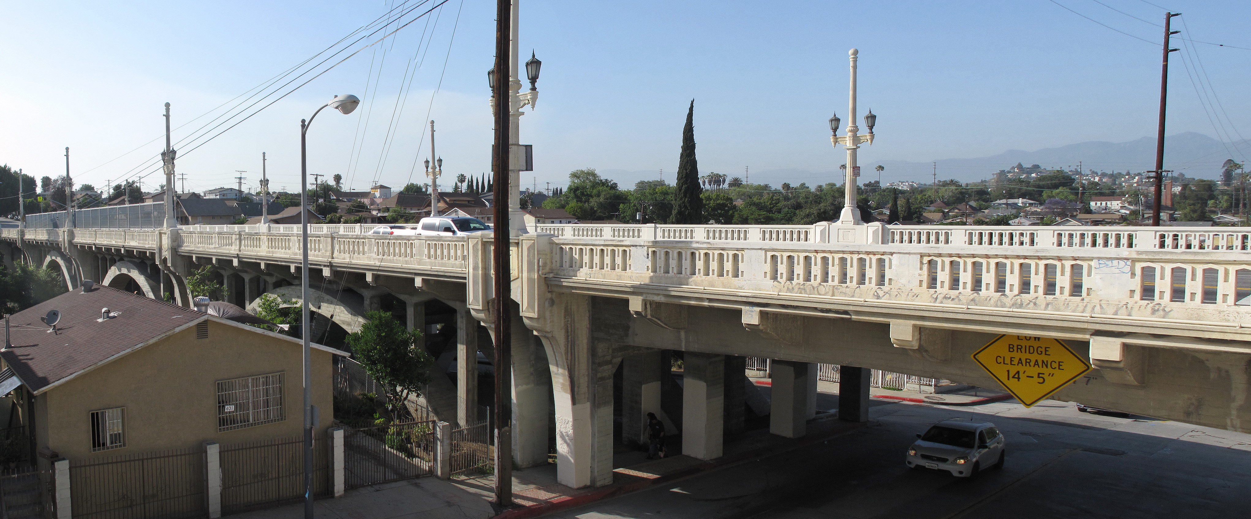 White concrete arch bridge with decorative balustrades and lamp posts in an urban neighborhood.