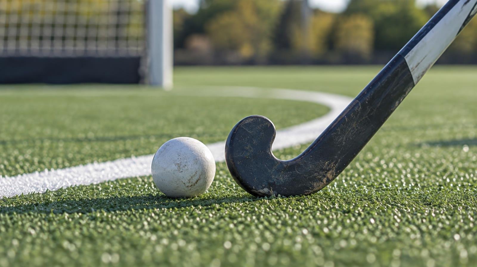 A field hockey stick and ball resting on green artificial turf near a painted line.