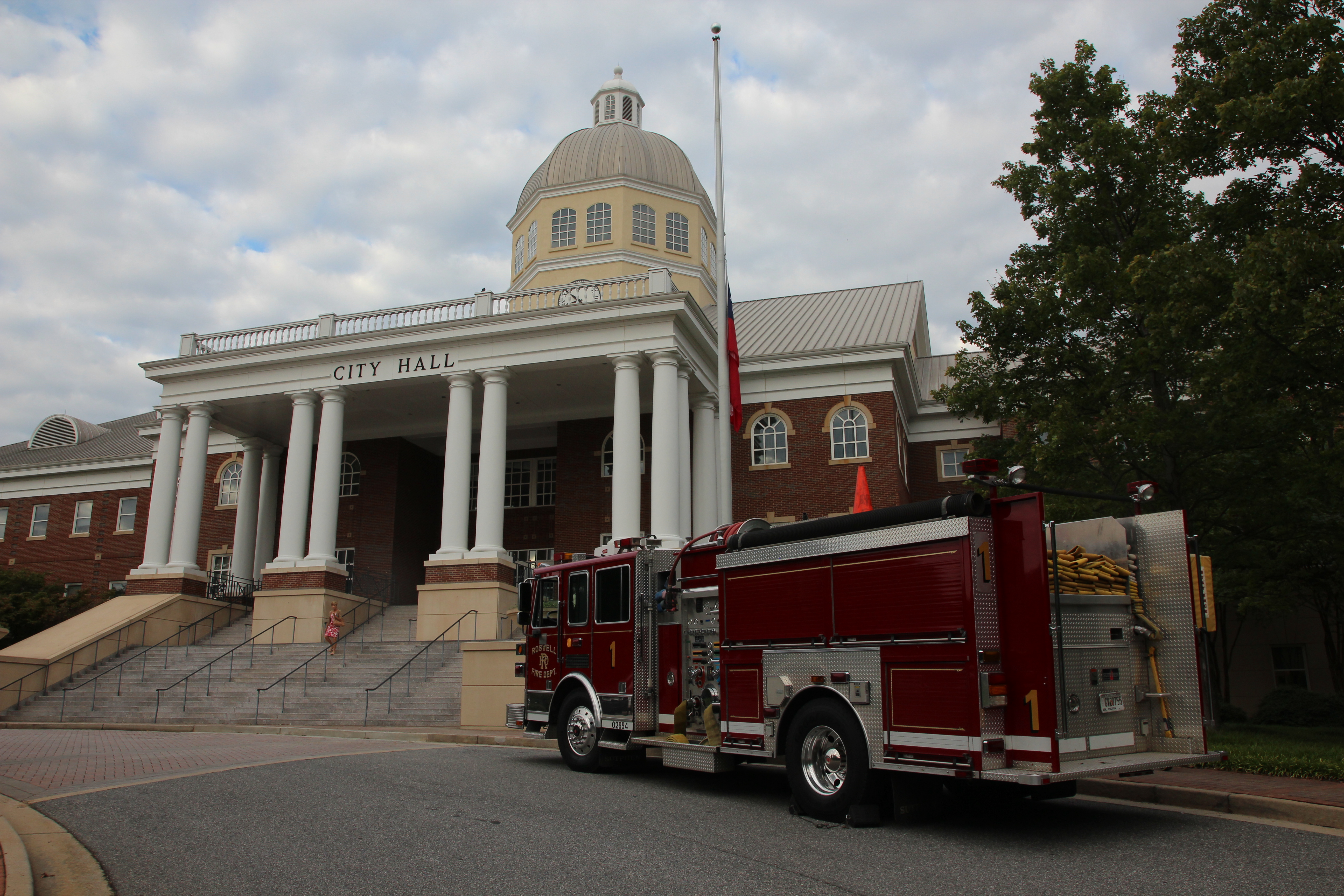 Neoclassical brick city hall with white columns, dome, and a red fire truck parked outside.