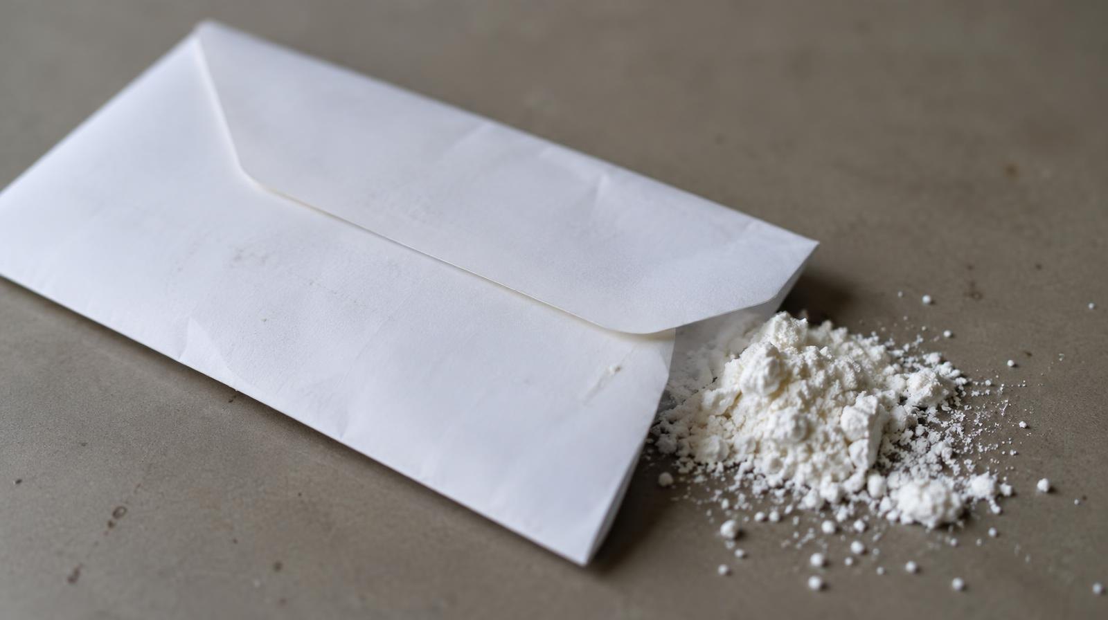 A white envelope with a small pile of white powder beside it on a plain surface.