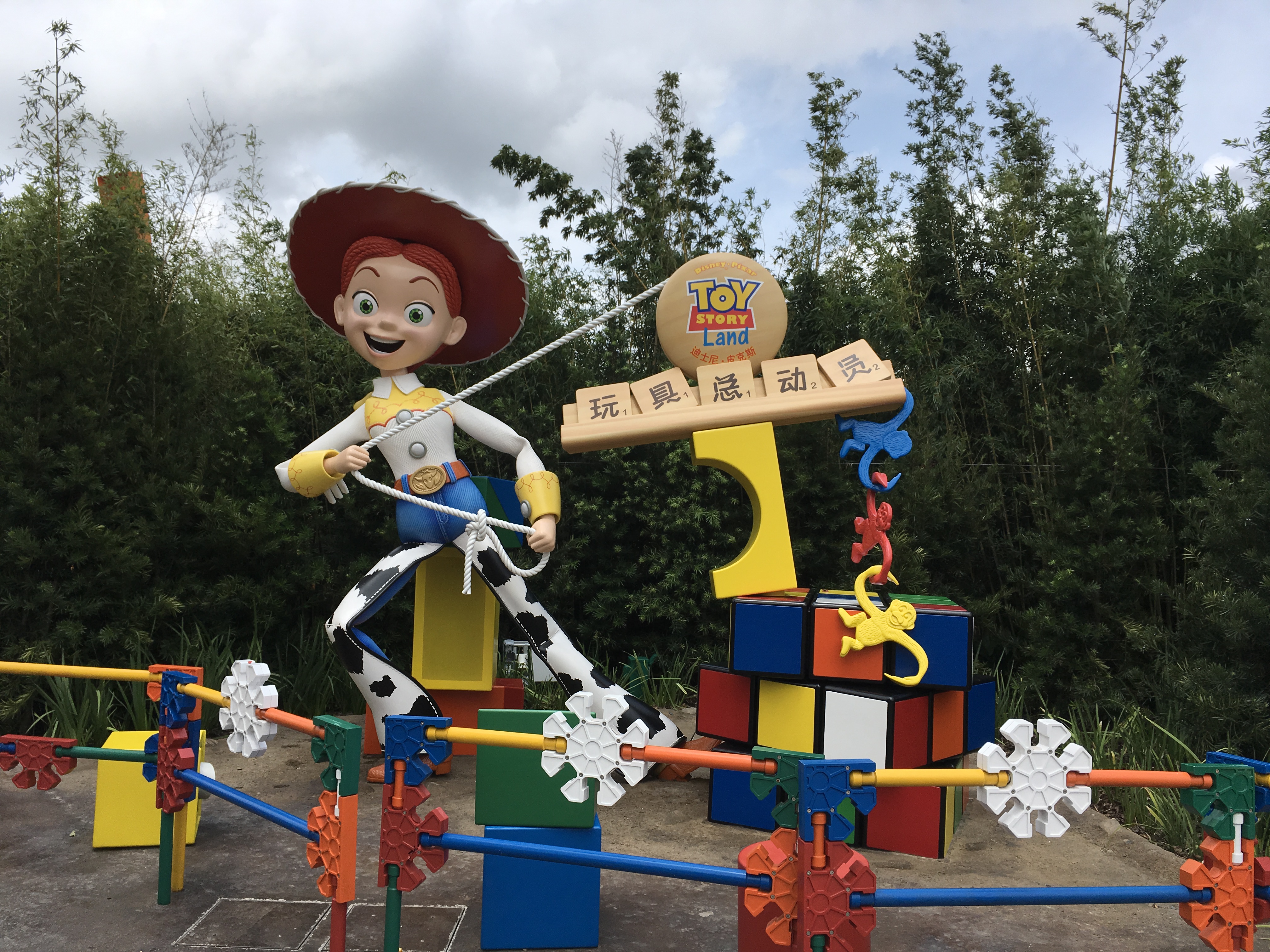 A large Jessie cowgirl statue stands at a Toy Story Land theme park entrance with toy-themed decorations.
