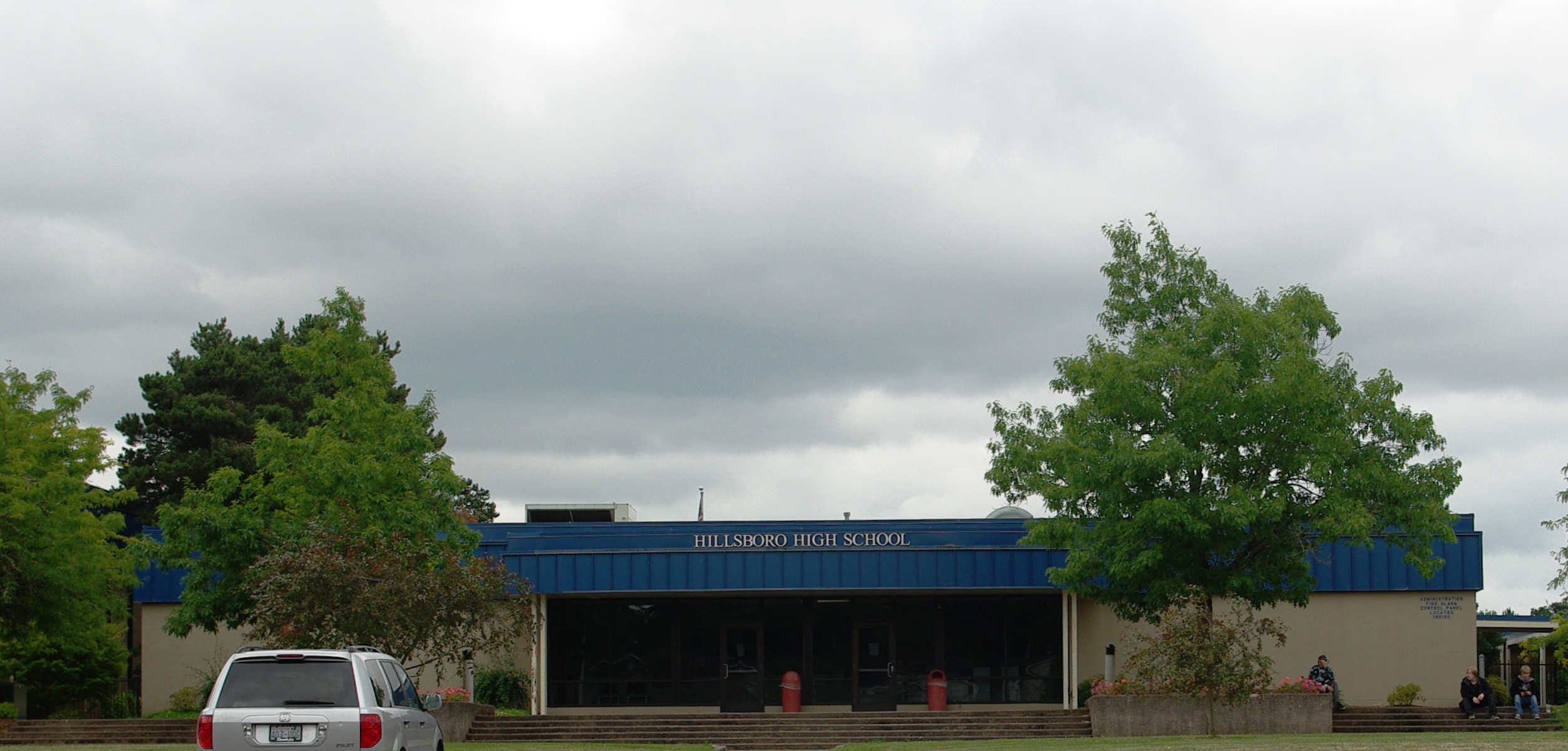 Exterior of a single-story school building with a blue awning and trees.