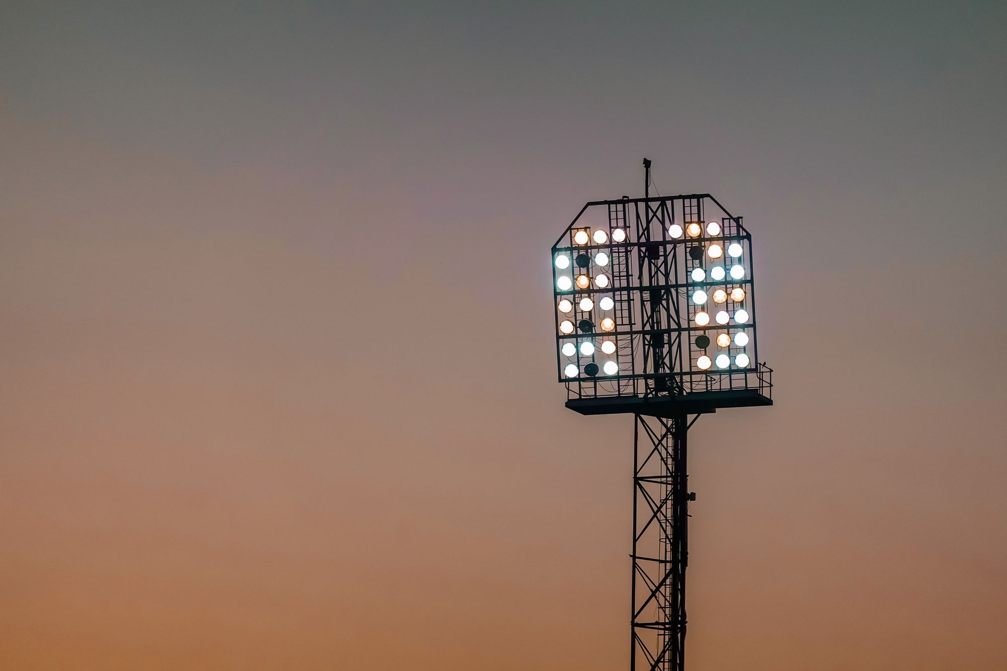 A detailed view of stadium floodlights set against a colorful sunset sky, highlighting sports venue ambience.