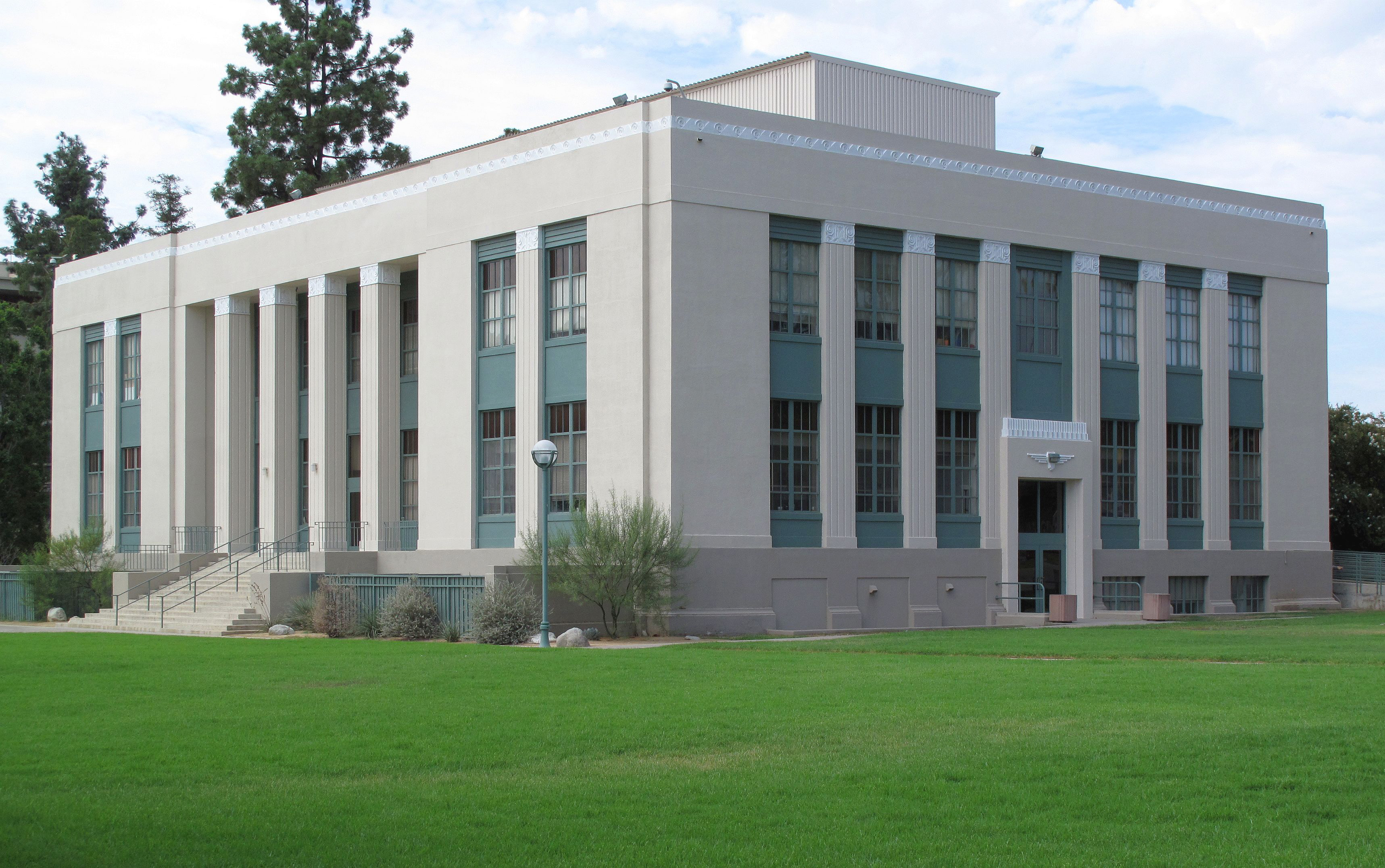 Multi-story college building with columns and large windows on a green lawn.