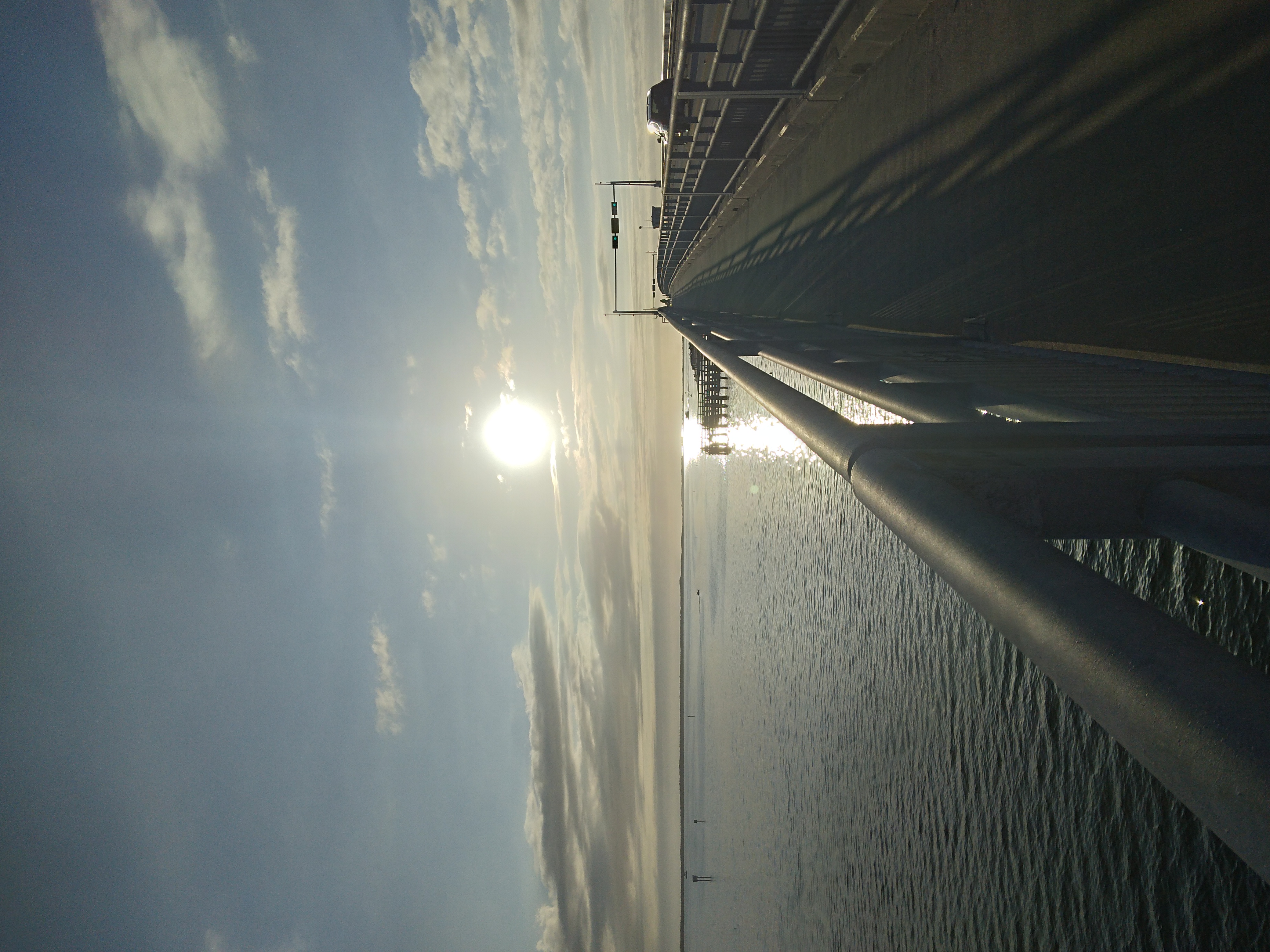 A long bridge extends over calm water toward a glowing sunset sky.