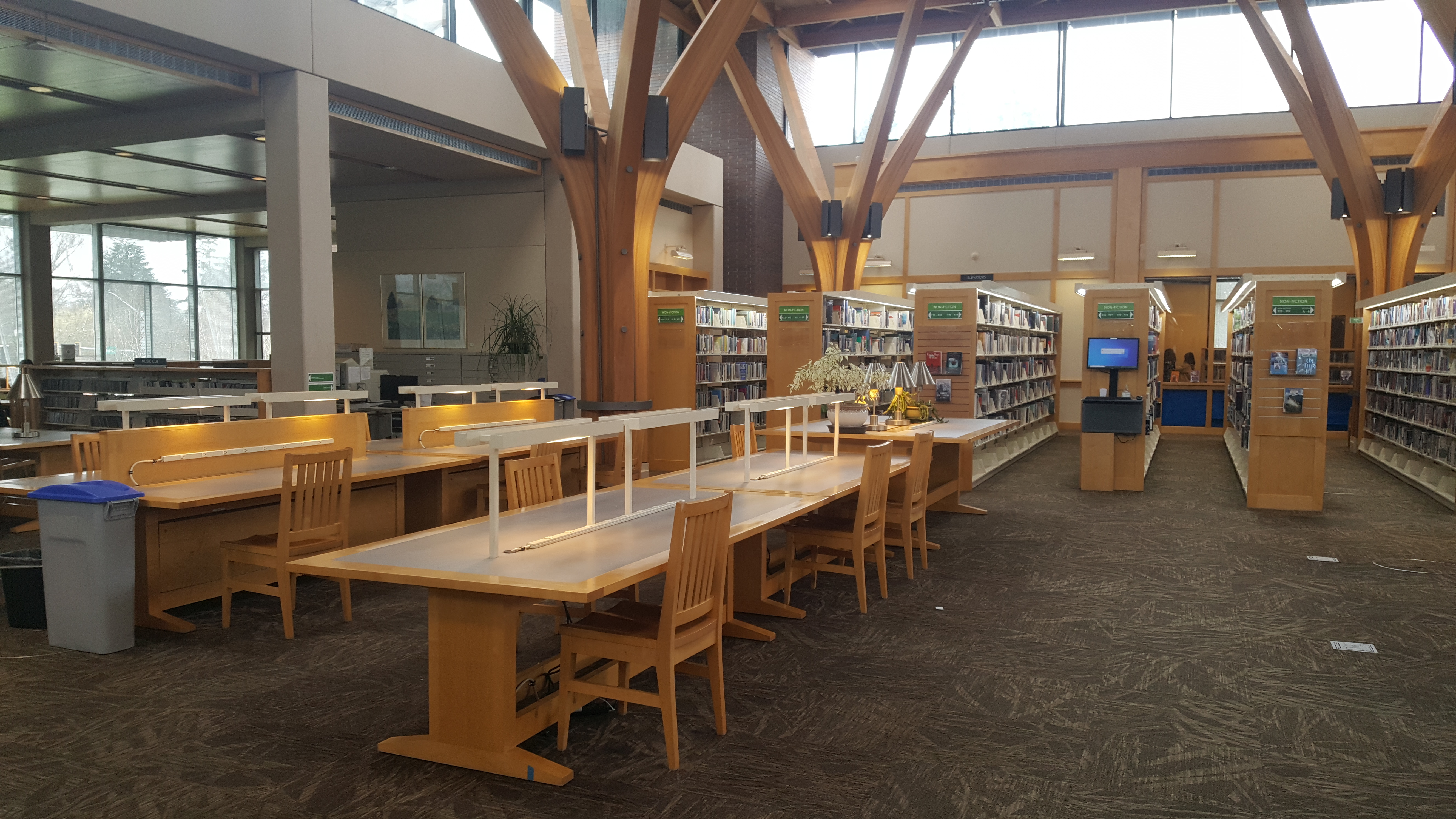 Library interior with high wooden beam ceiling, study tables, and bookshelves in the background.