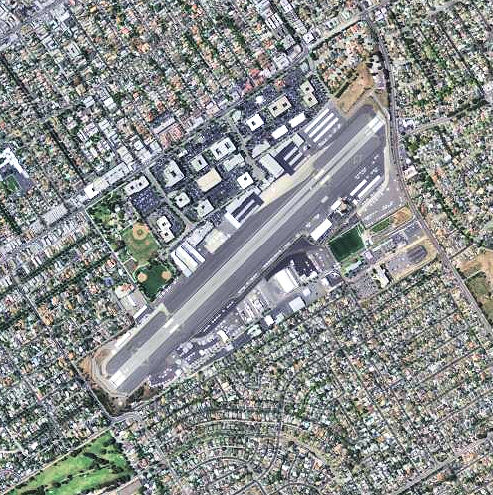 Aerial view of an airport runway surrounded by dense urban residential neighborhoods.