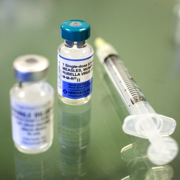 Two small glass vaccine vials and a capped syringe on a reflective surface.