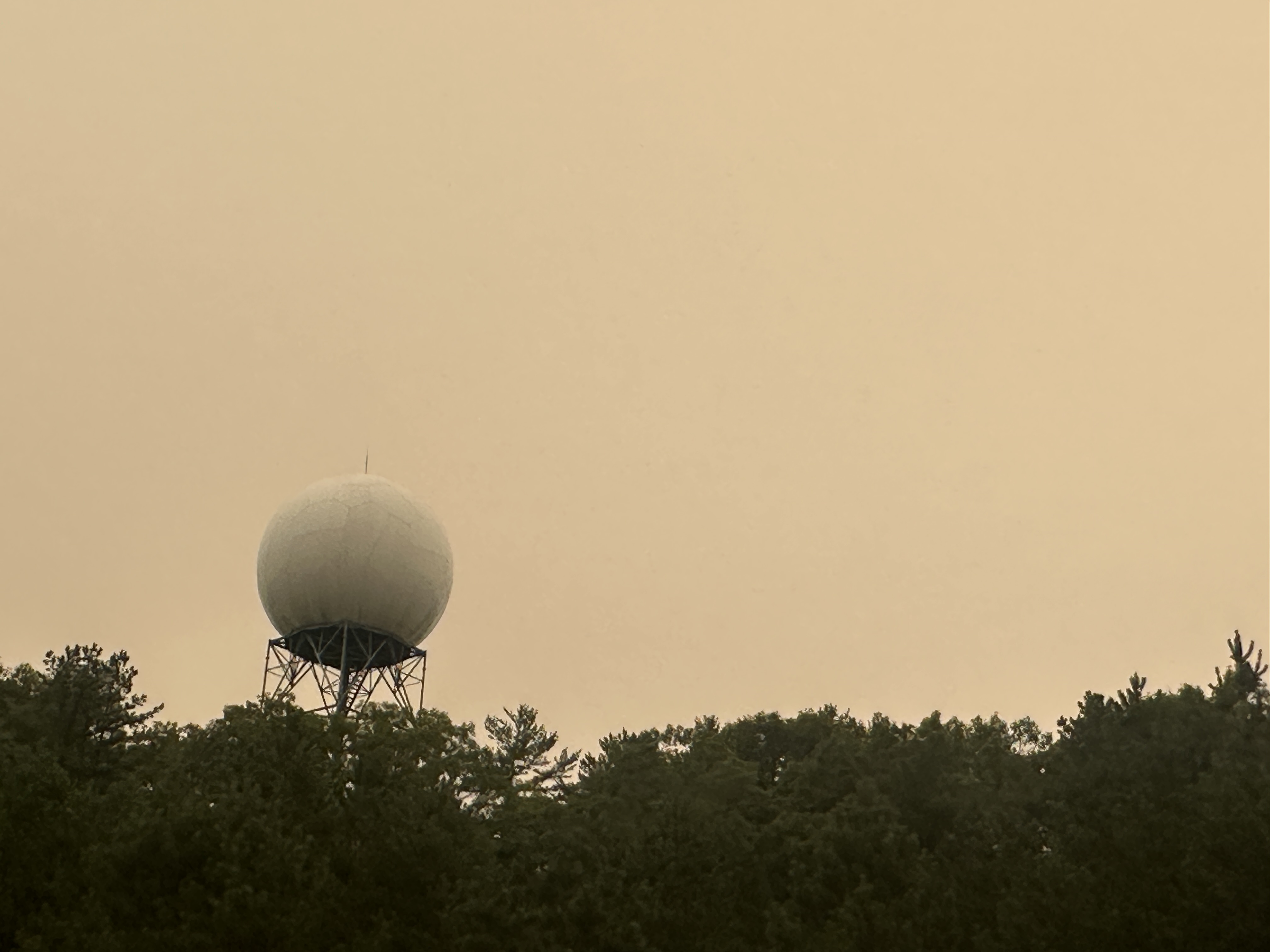 Weather radar dome rising above trees under a thick yellowish-brown hazy sky.