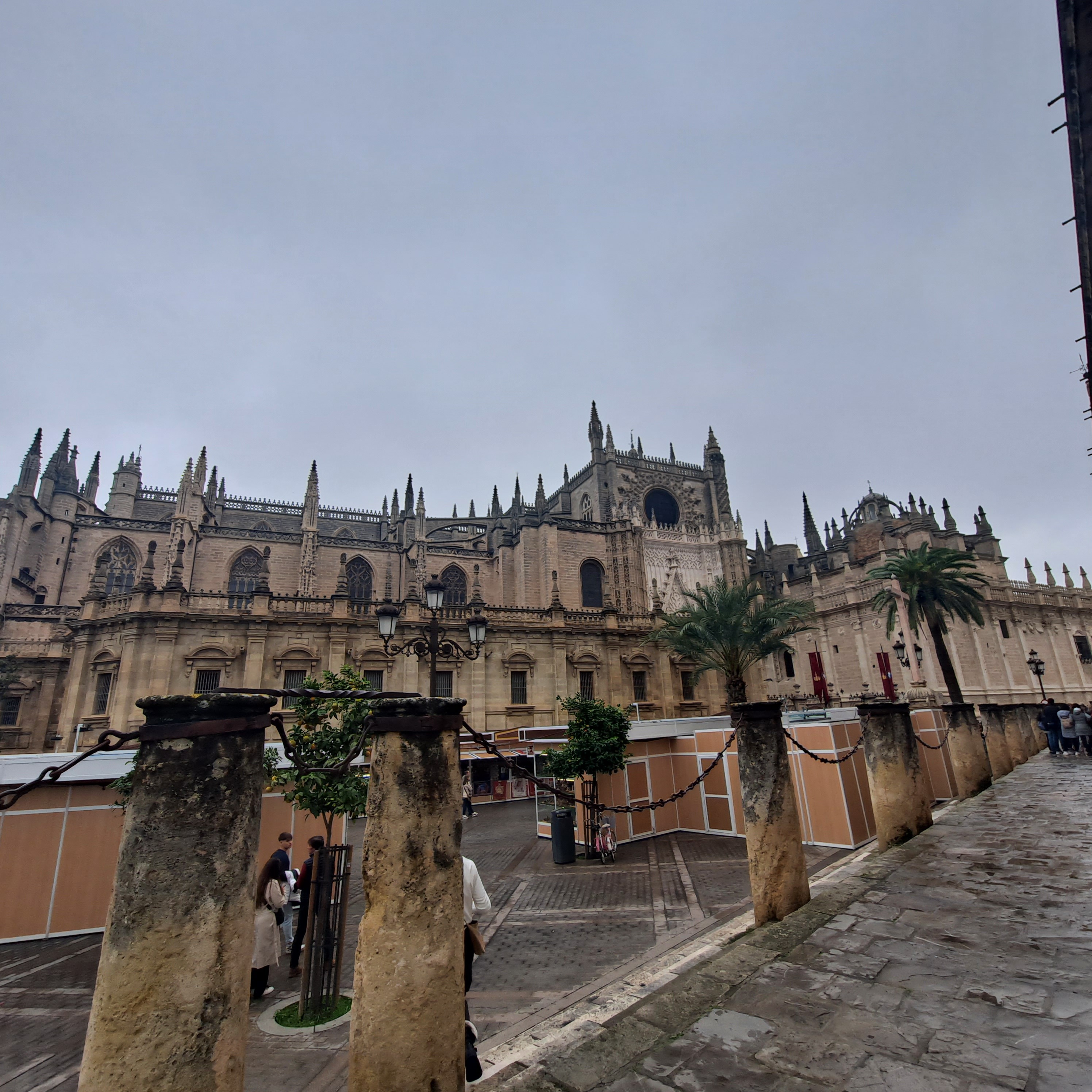 Gothic cathedral with ornate spires seen from a plaza with palm trees and stone columns.