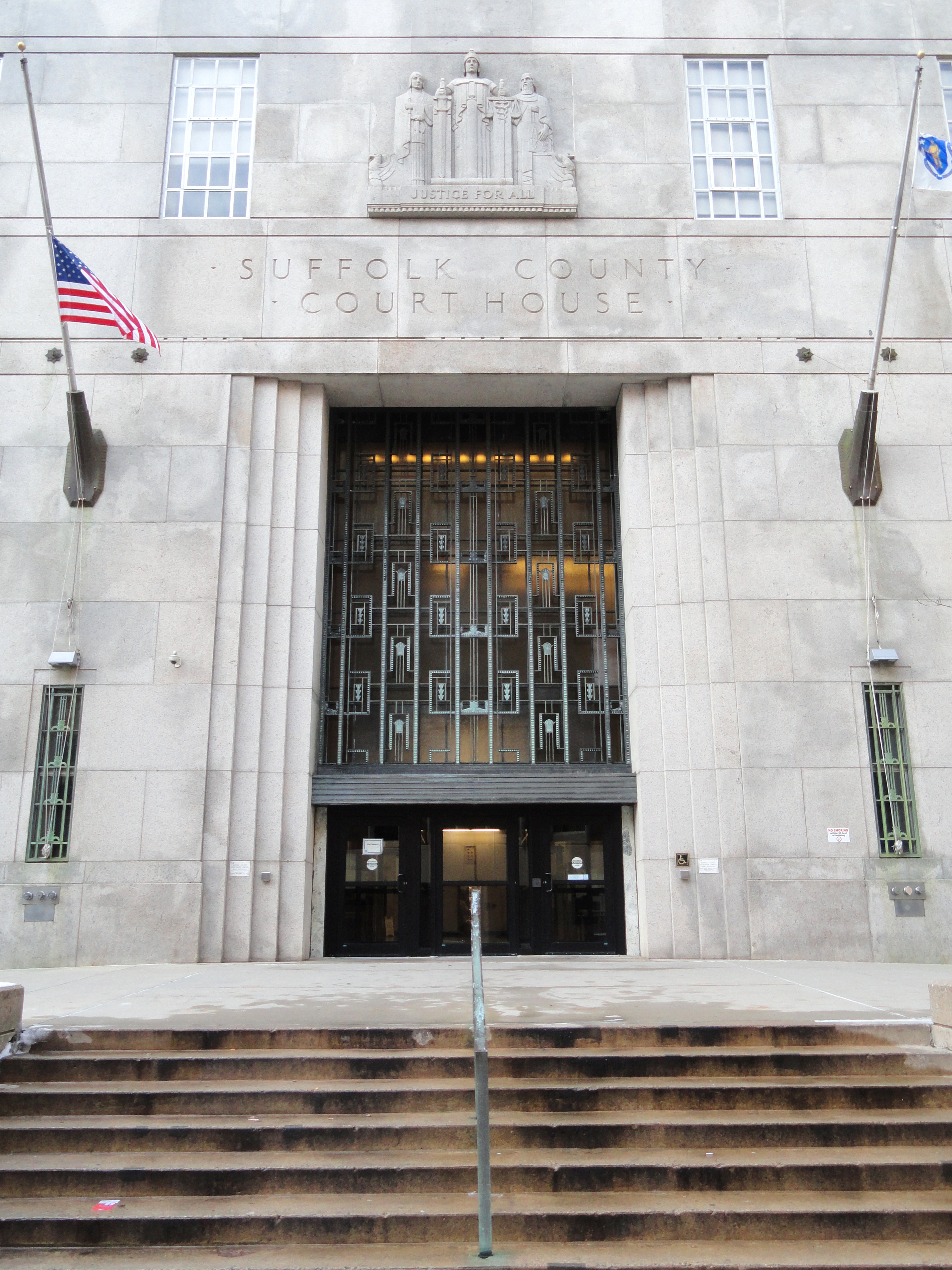Stone Art Deco courthouse entrance with large metal doors and American flag.