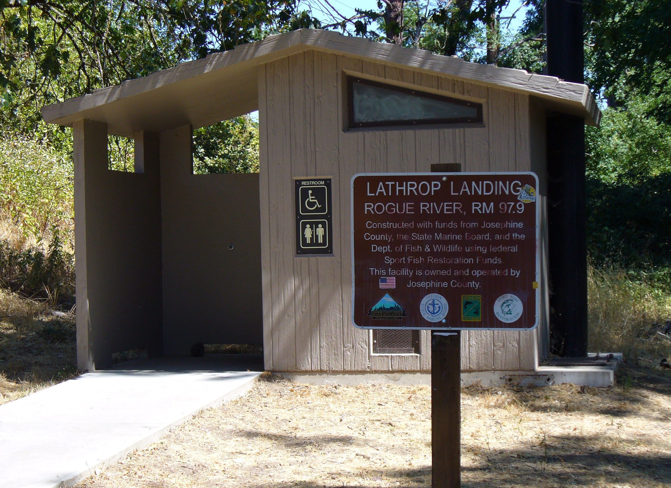 A small modular public restroom building with covered entrance and ADA signage beside a paved path.