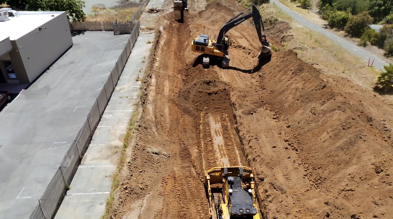 Aerial view of a bulldozer and excavator digging a trench at a construction site.