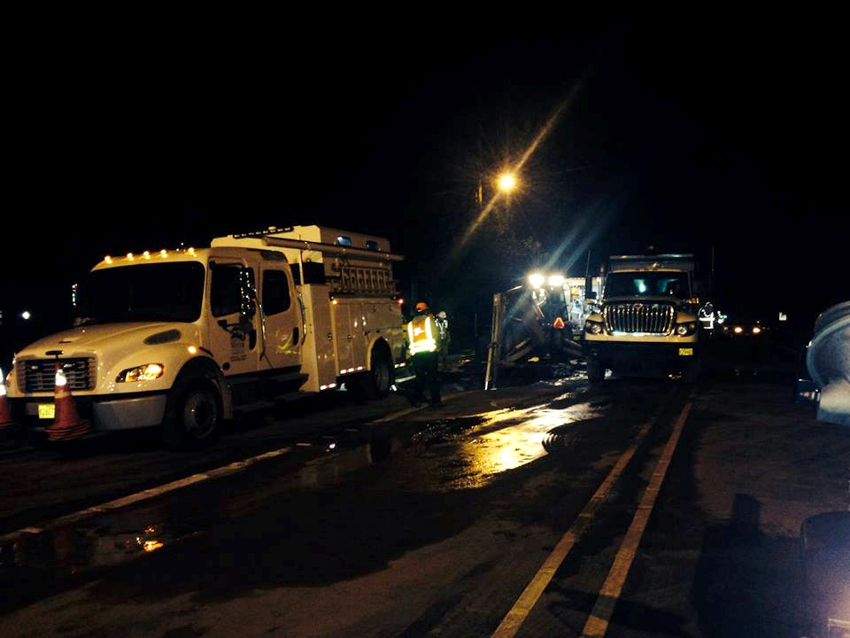 Utility trucks and workers in reflective vests on a wet road at night.