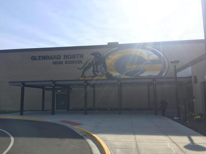 Exterior entrance of a brick high school with name signage and a painted panther mascot mural.