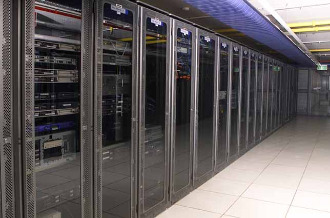 Rows of server racks in glass-fronted cabinets inside a data center aisle.