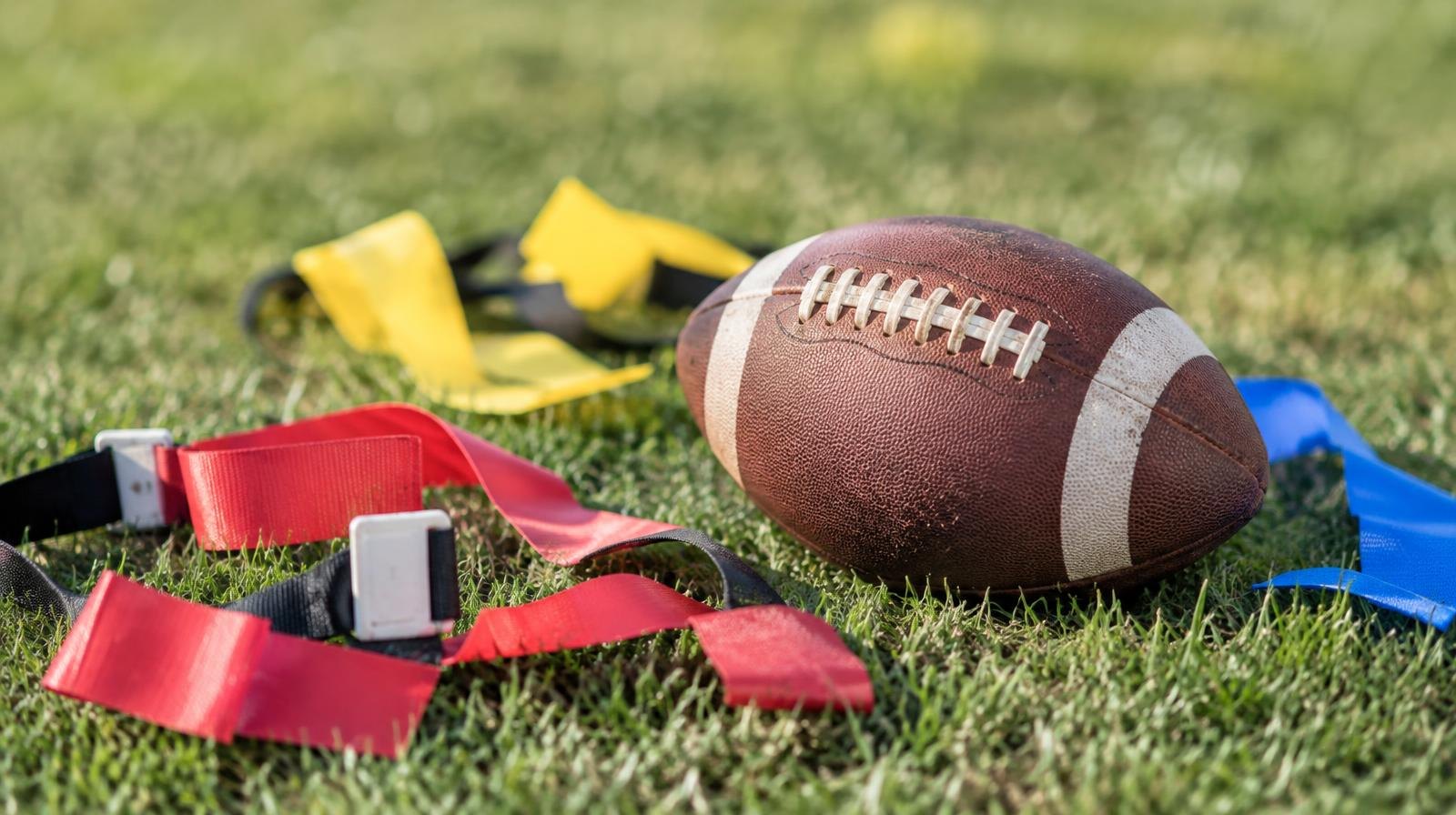 A football and colorful flag belts lying on a green grass field in sunlight.
