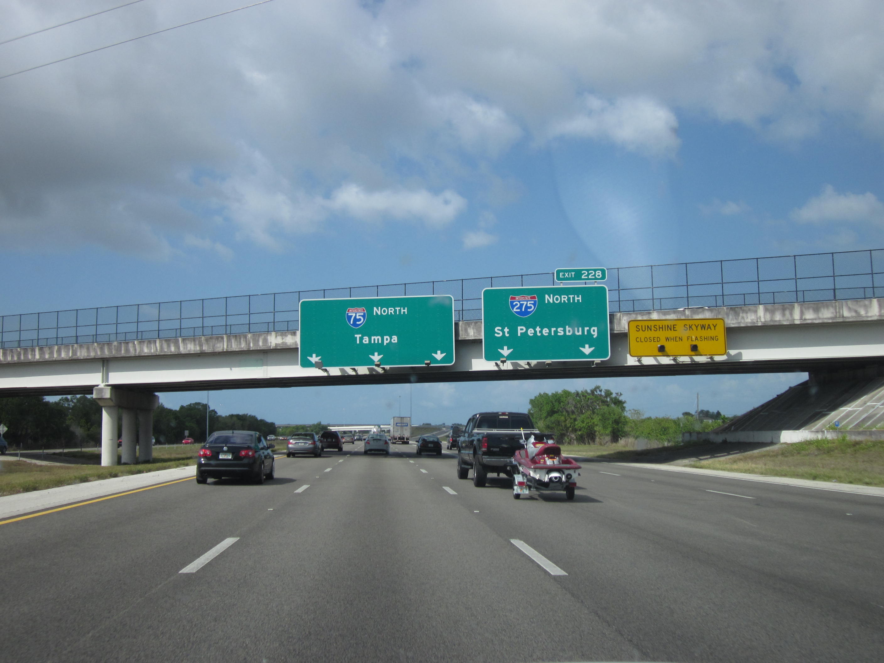Multi-lane Interstate 75 in Florida with green overhead signs and an overpass bridge in the distance.