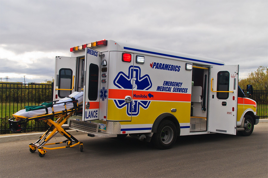 Ambulance rear doors open with a powered stretcher extended on the ground beside it.