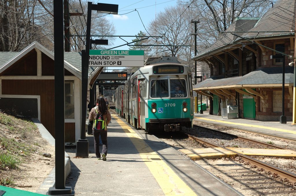 An inbound MBTA Green Line train arriving at Newton Highlands station with the historic building visible at right.
