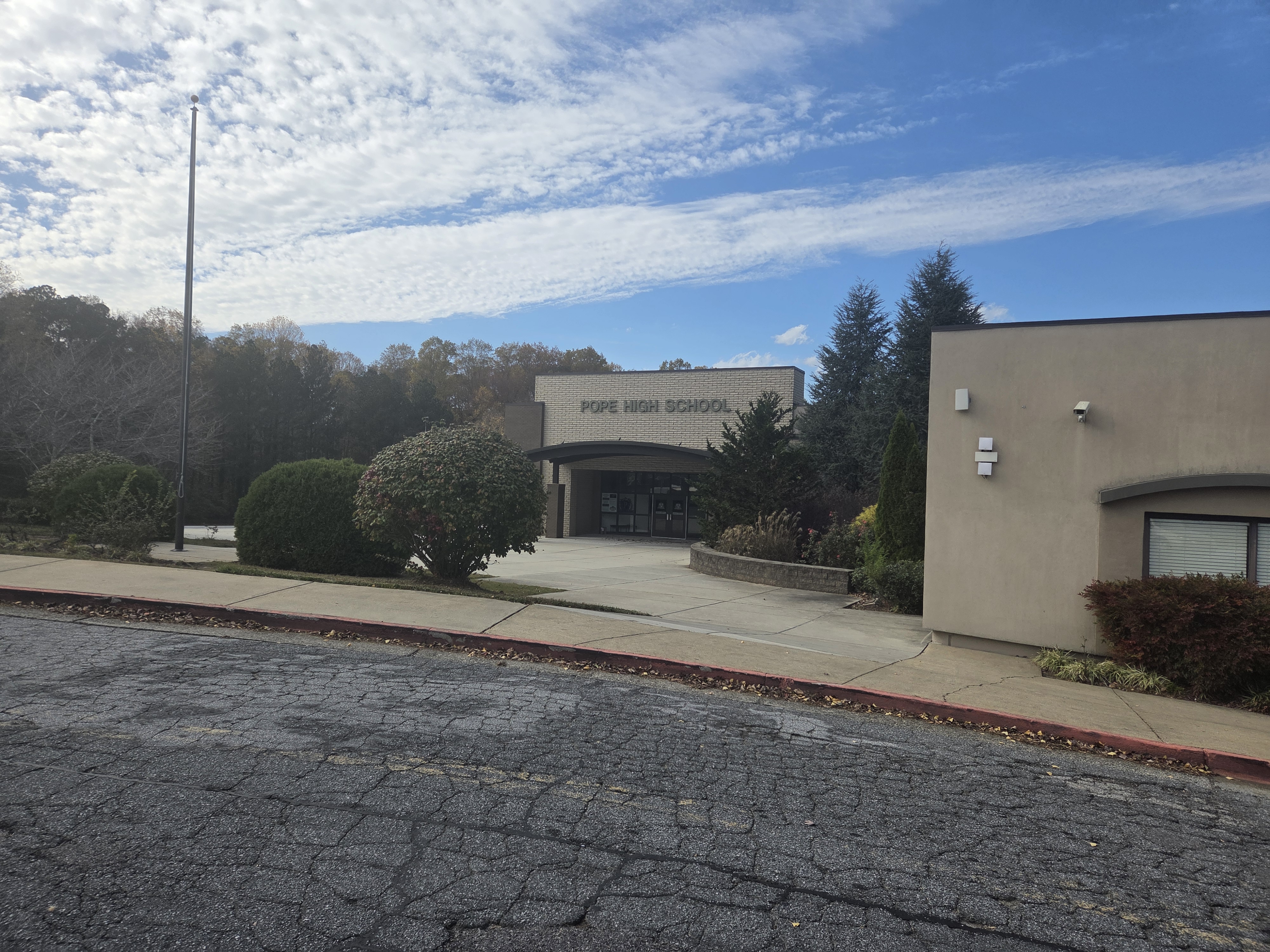 Exterior entryway of a tan stucco high school building with signage and landscaping.