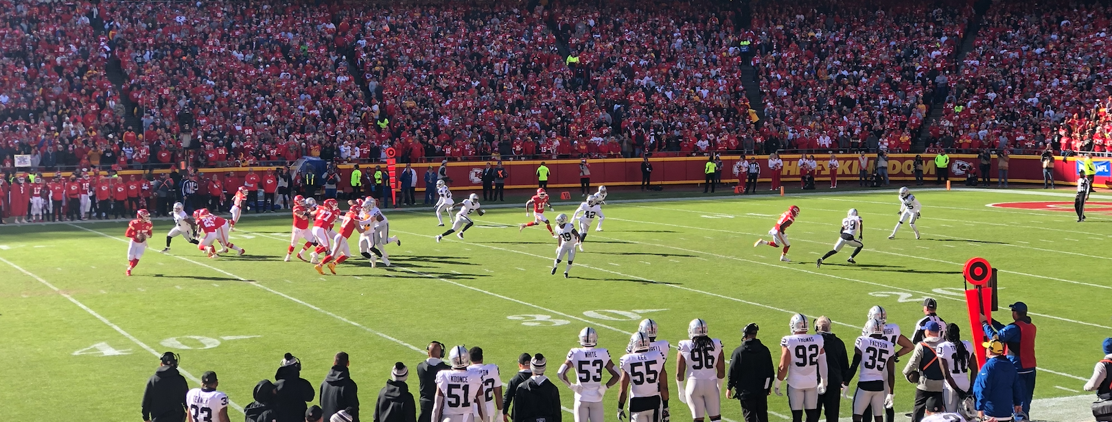 Football players on a field at a packed NFL stadium with fans in red in the stands.