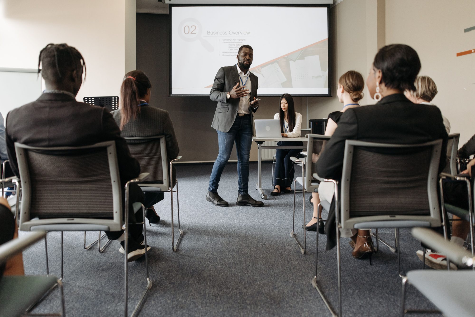 A group attending a business seminar with a presenter and screen display.