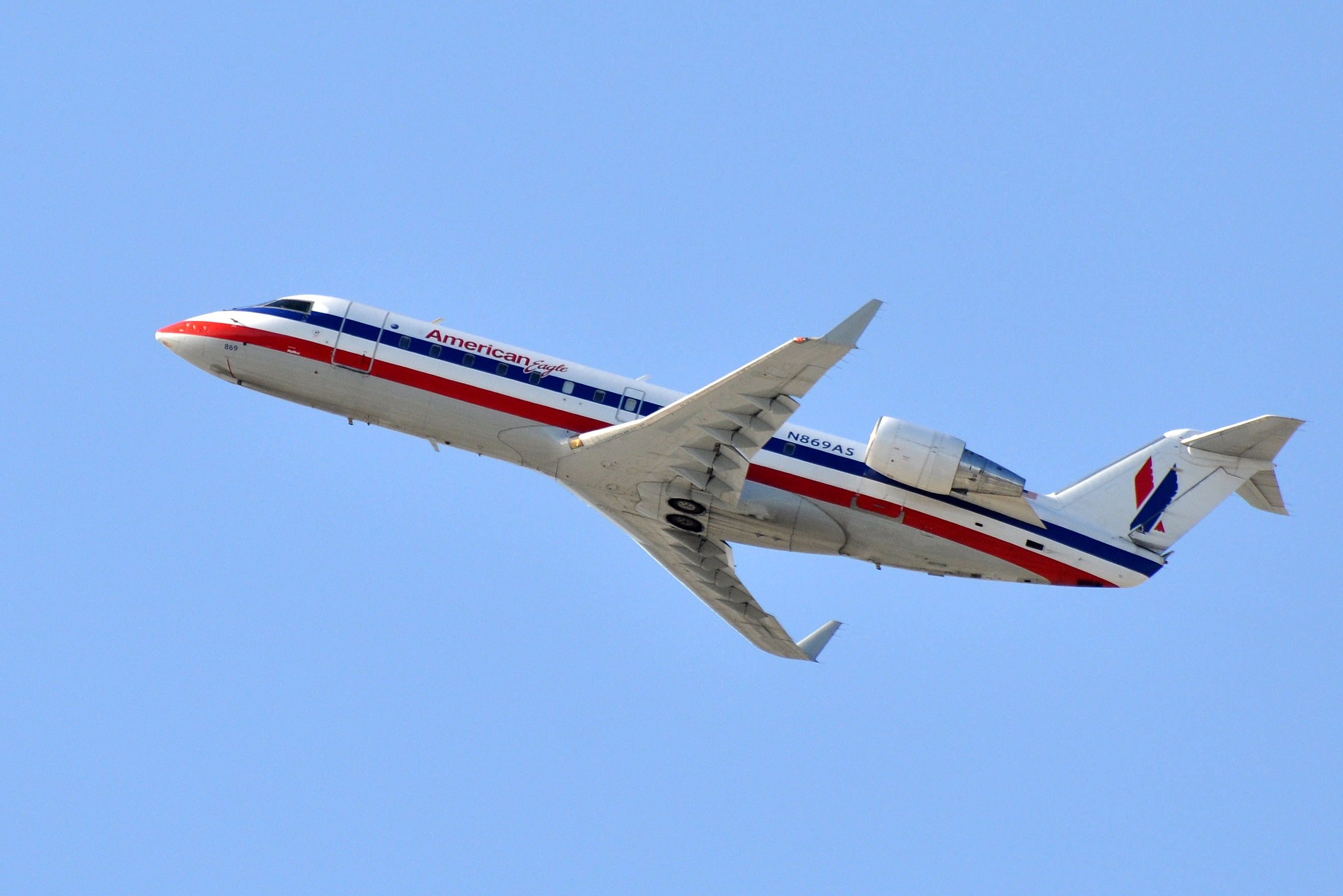 Regional jet aircraft climbing in flight against a clear blue sky.