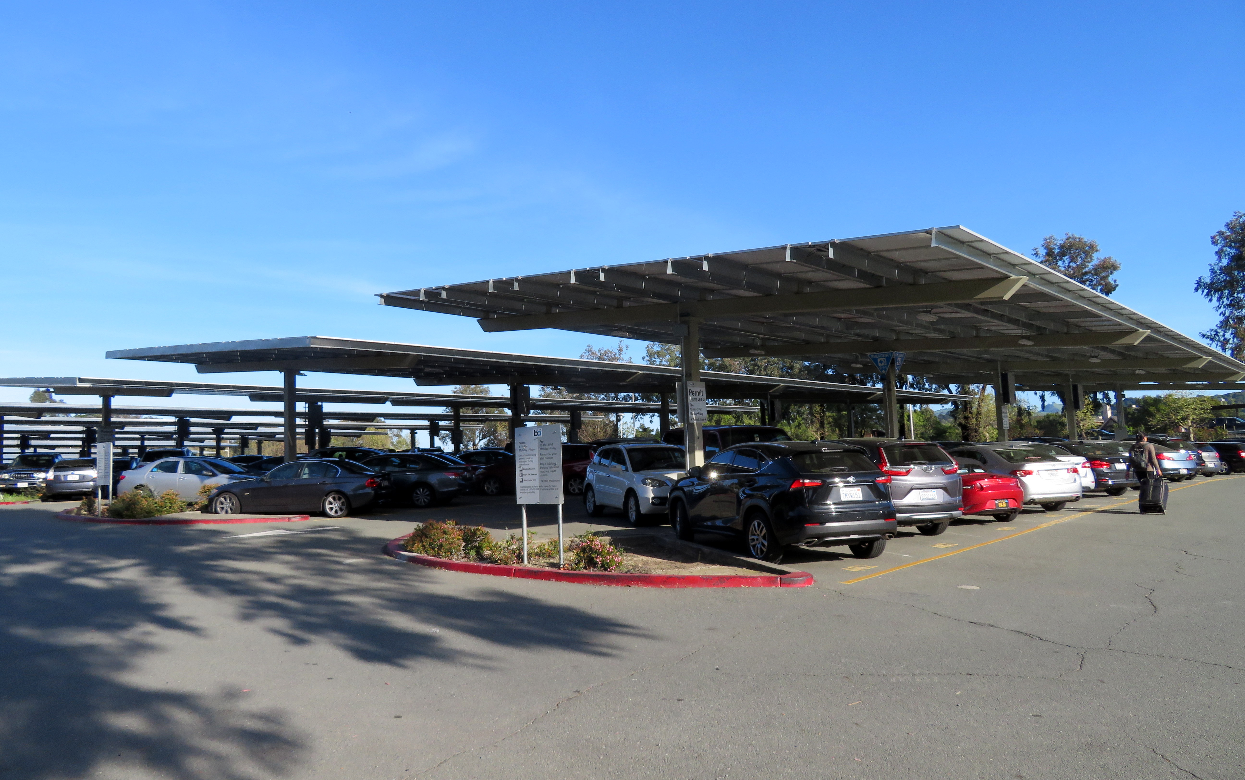 Solar panel canopy covering a parking lot filled with cars under a blue sky.