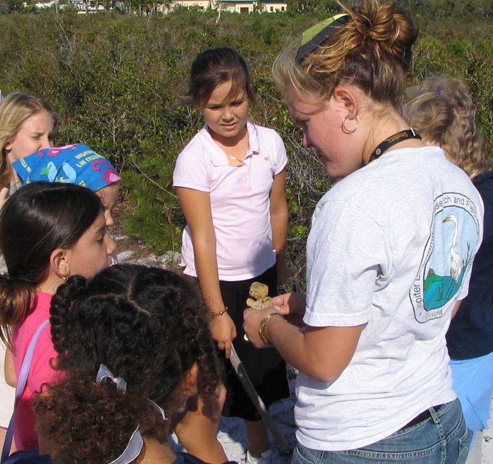 Students and an adult gather outdoors around native shrubs during an environmental field activity.