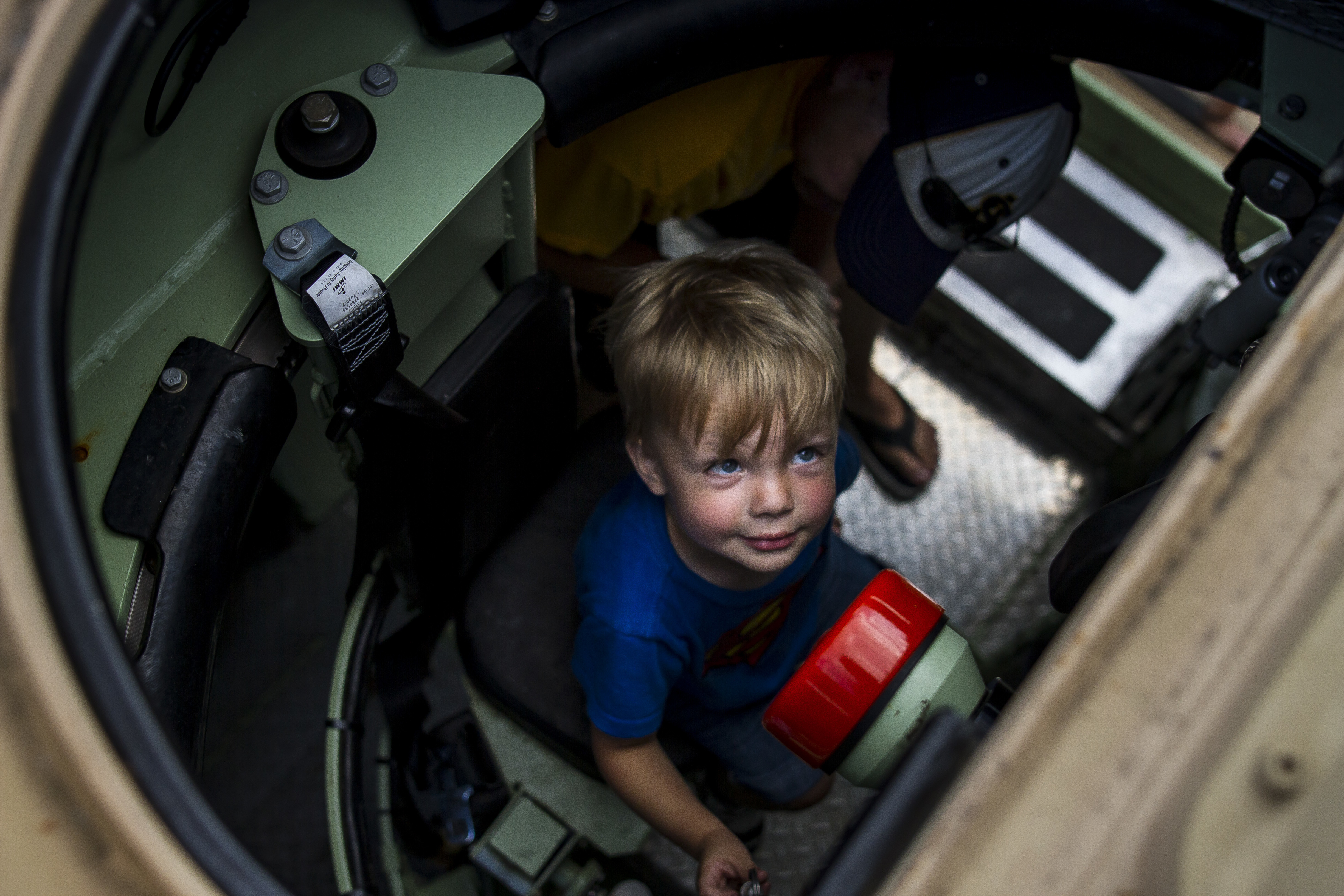 A young boy peers up from inside the open hatch of a military armored vehicle.