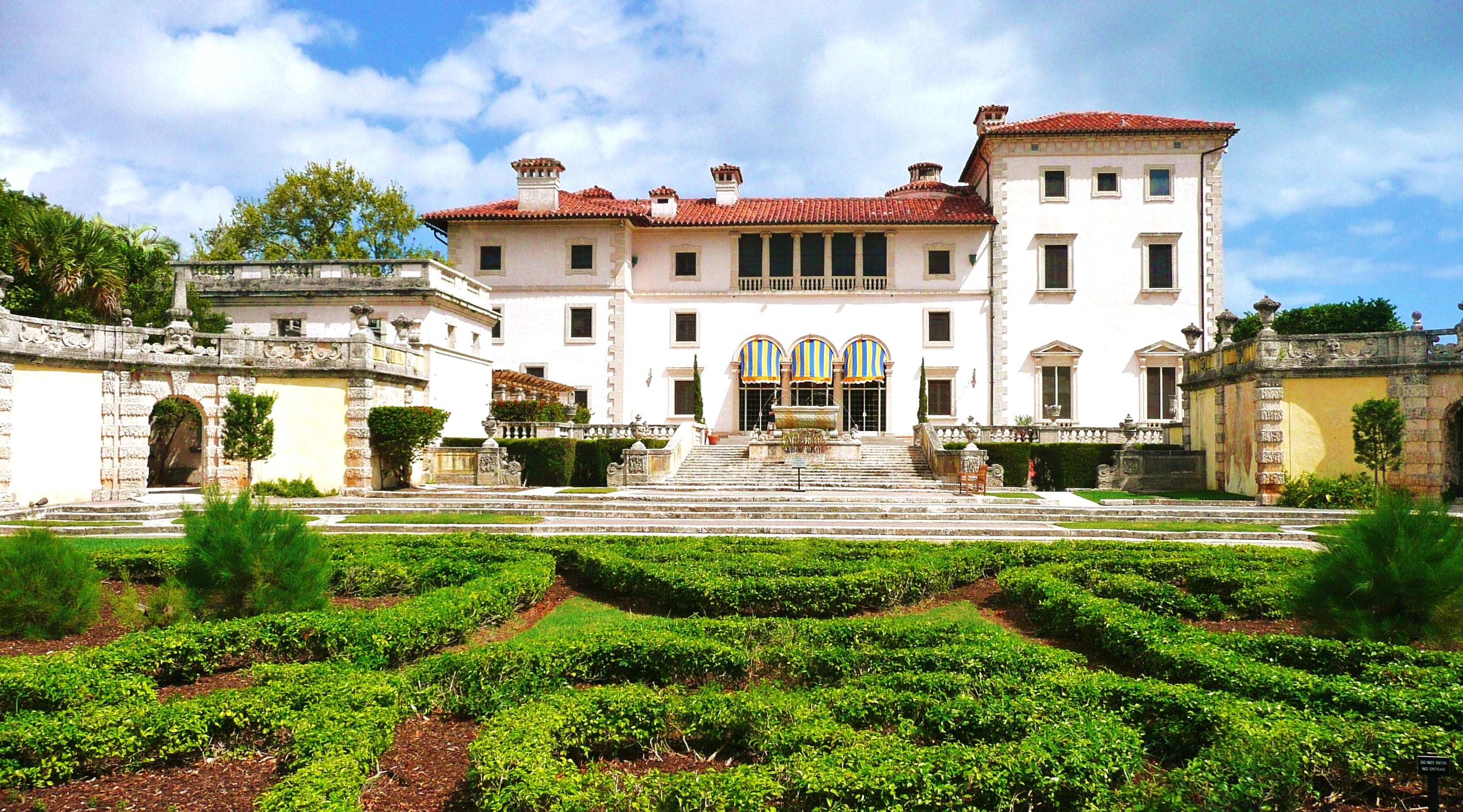 White Italian Renaissance villa with red tile roof and formal hedged gardens.