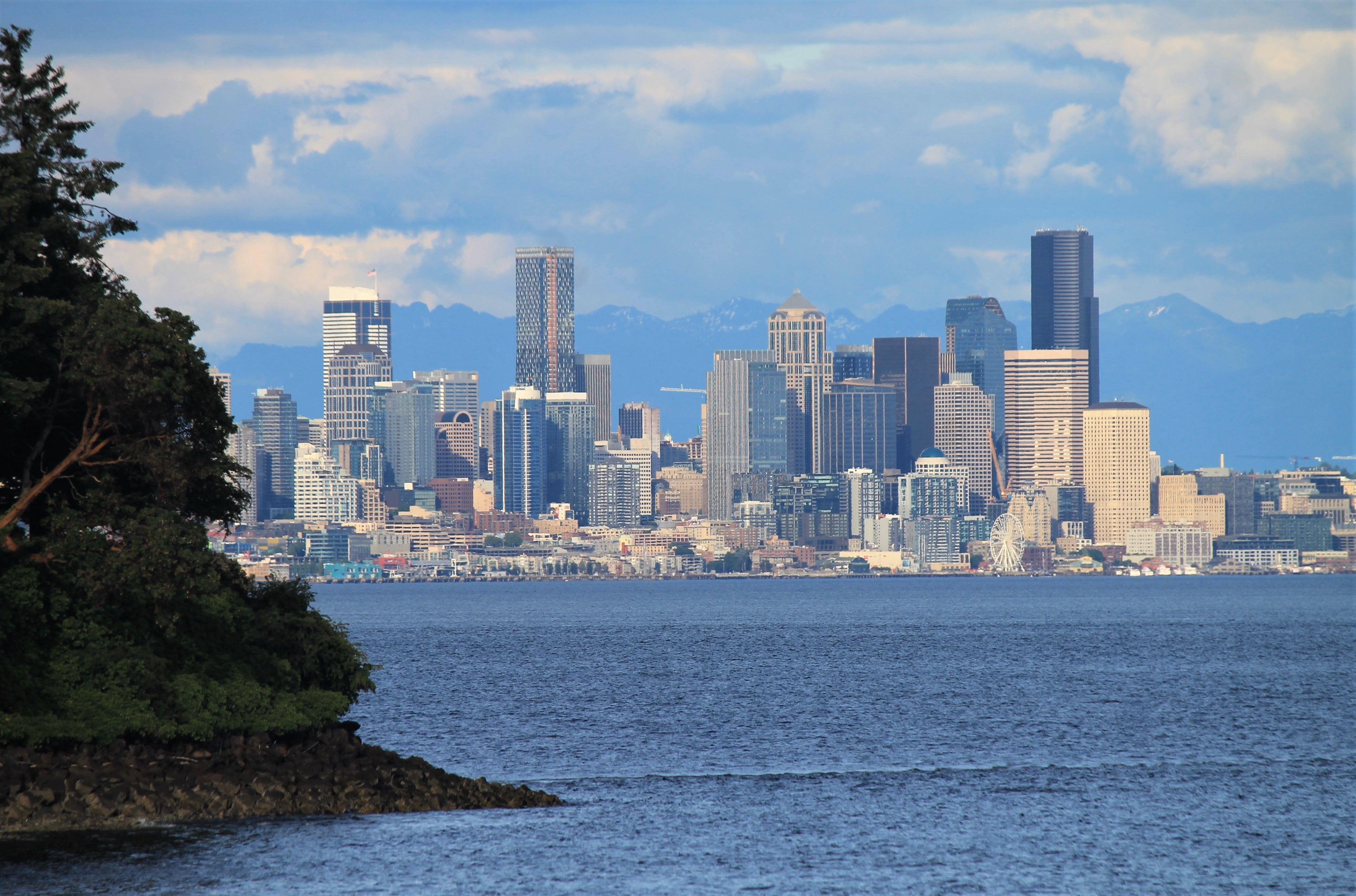 Downtown Seattle skyline with high-rise buildings reflected across Puget Sound, mountains behind.