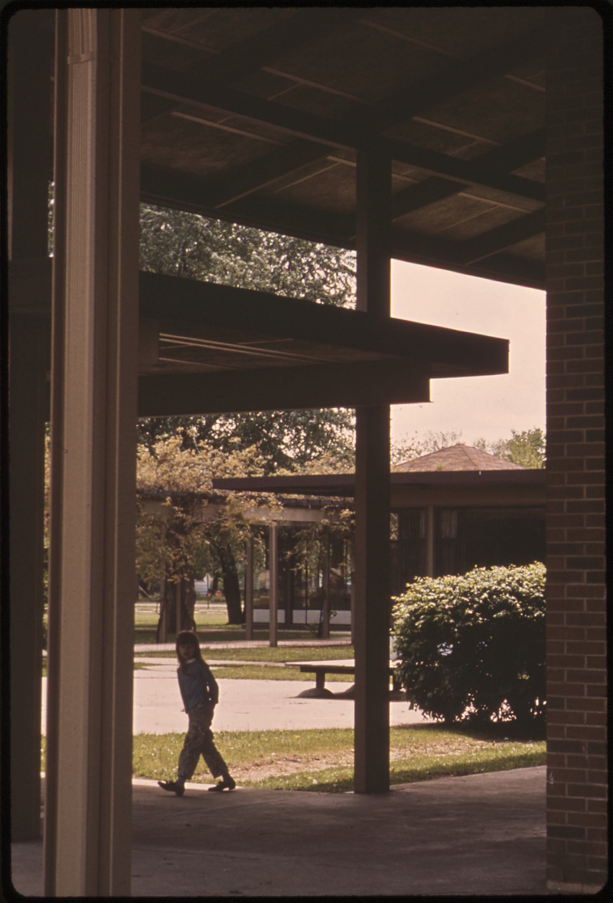Person walking through a covered outdoor corridor of a brick elementary school campus.